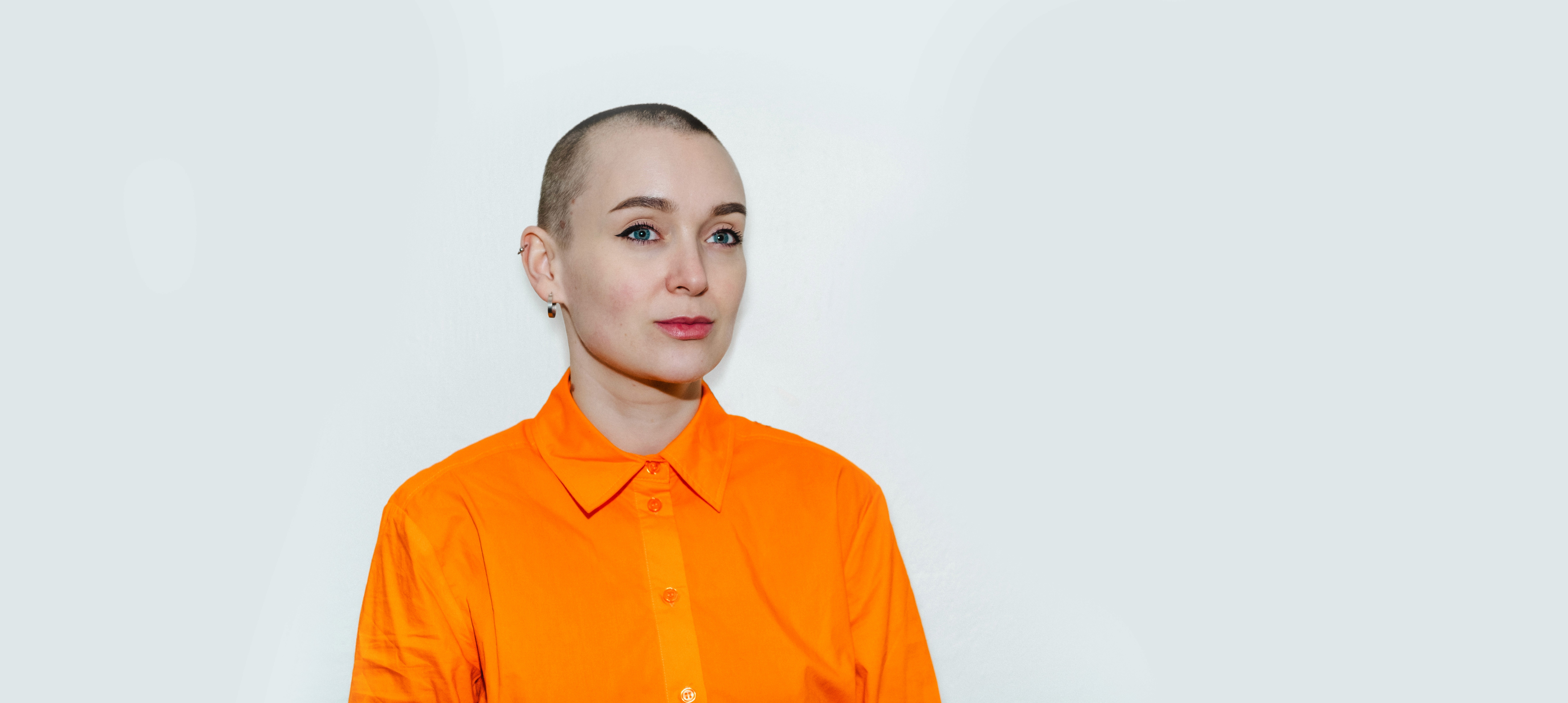 Portrett av designer Kristin Skårdal, ikledd orange skjorte på lys blåhvit bakgrunn