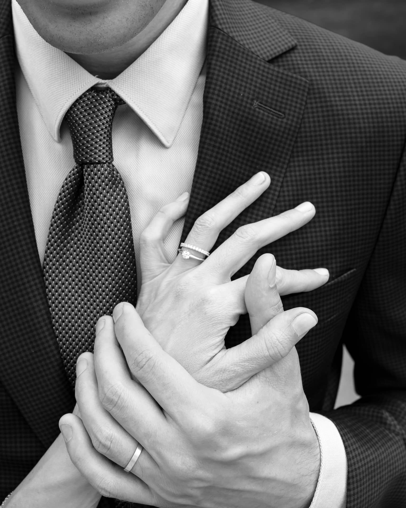 Editorial-style black and white couple portrait featuring hands, wedding rings and tailored suit details