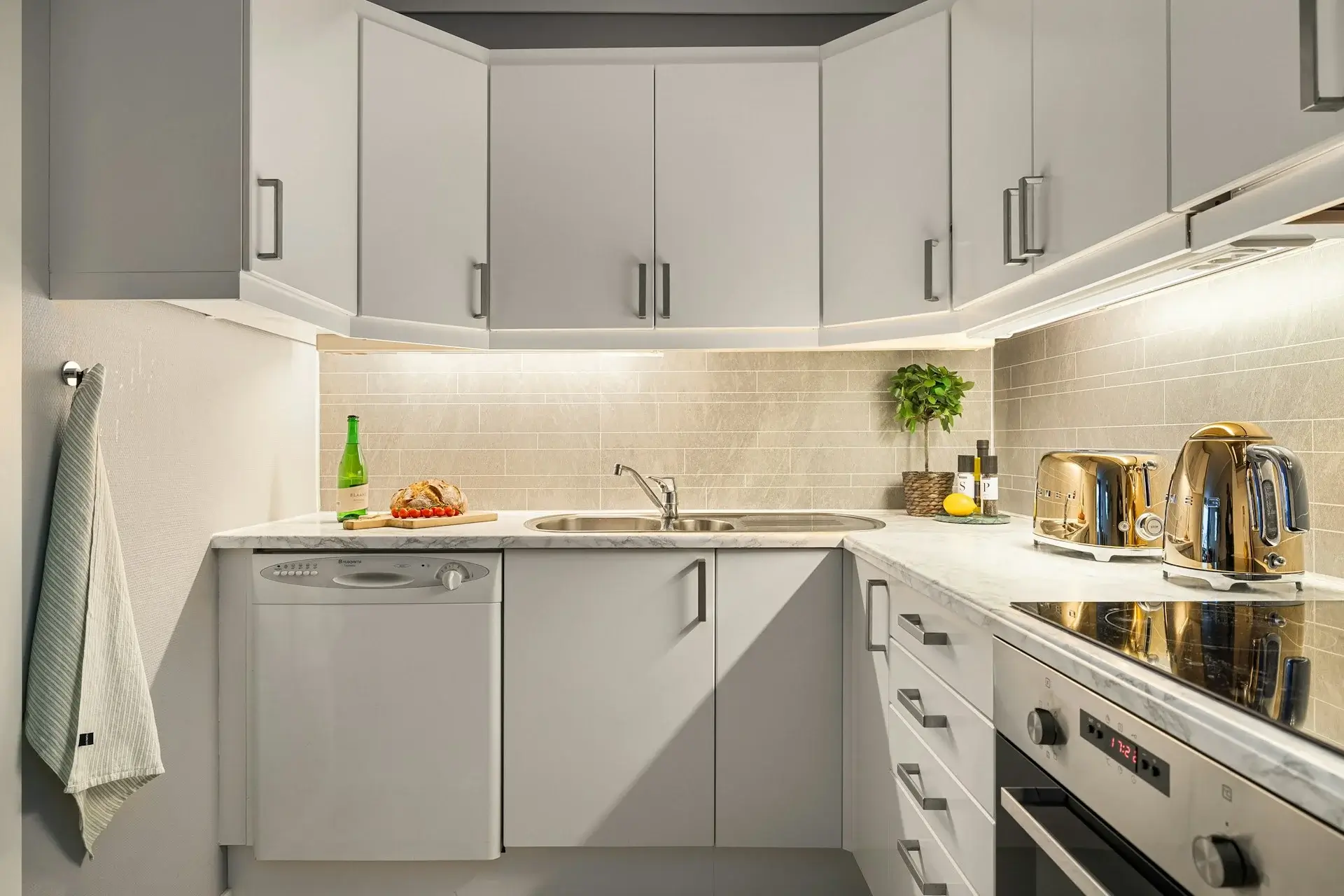 Modern white kitchen with marble countertops and built-in appliances.