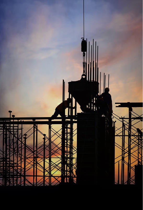 Silhouette of a person standing on a balcony with a city skyline at sunset, featuring vibrant hues in the sky.