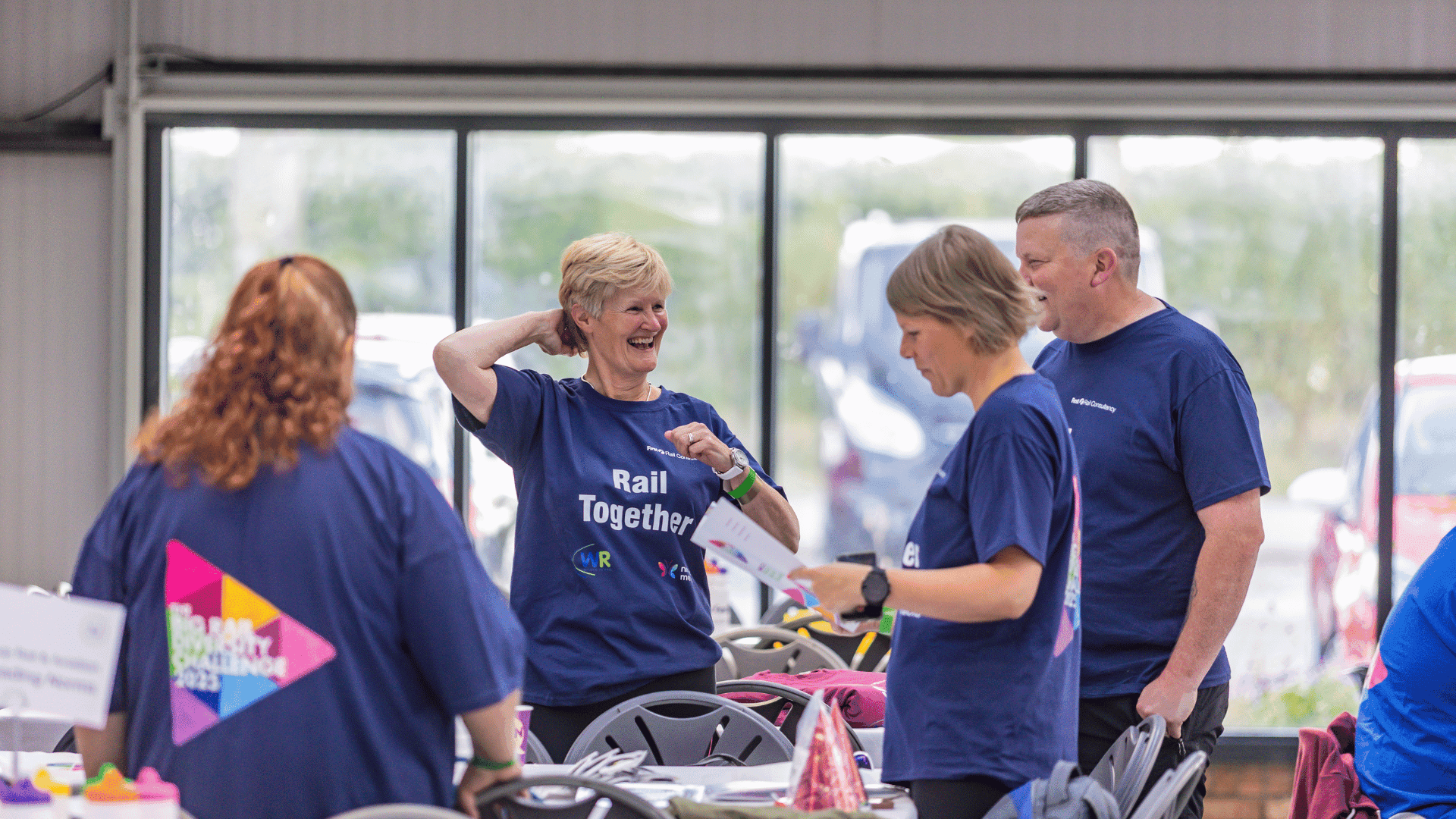 Outdoor team-building event with participants wearing matching blue shirts, taking part in inflatable obstacle courses and games, smiling and cheering, with the words 'ENTER A TEAM' in large bold white and green text across the image.