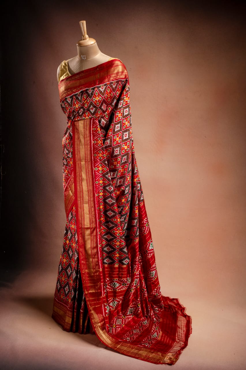 An orange Ikat saree from That Saree Shop draped on a mannequin, displaying its handwoven geometric patterns and rich traditional craftsmanship in vibrant hues.