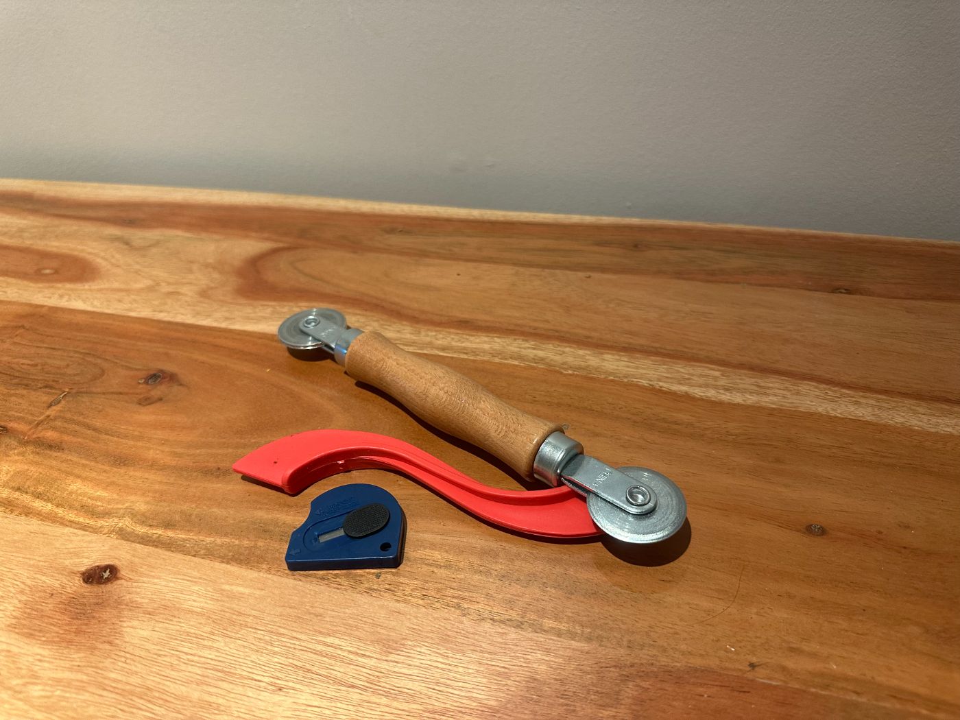 Kit de réparation de moustiquaire avec outil à roulette double, rouleau de serrage rouge et coupe-filet bleu, sur table en bois