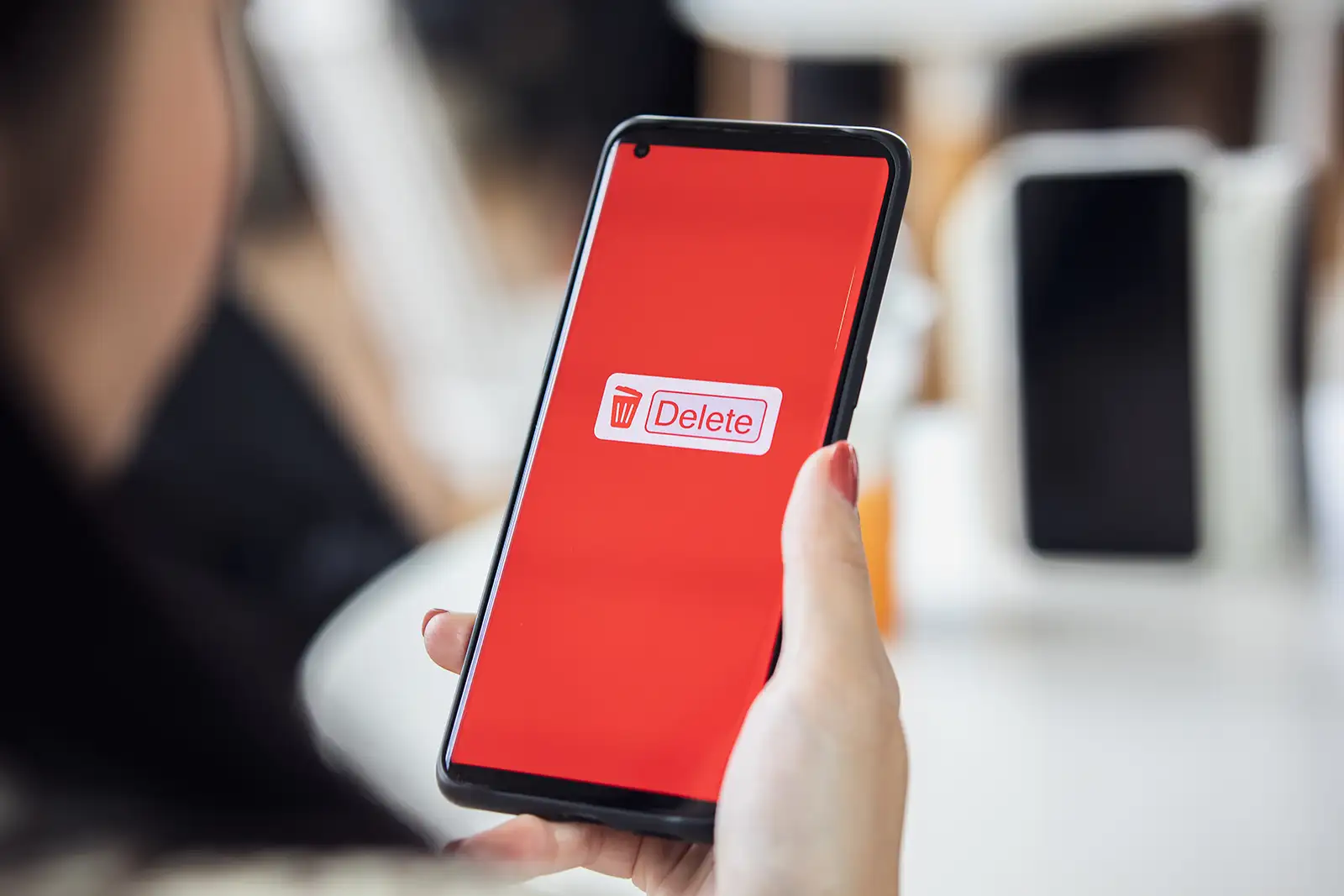 Person holding a phone displaying a red screen with a Delete button in the center