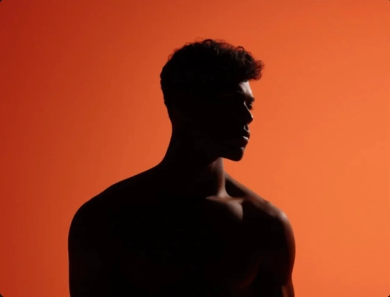 Silhouette of a man in profile against a bright orange background