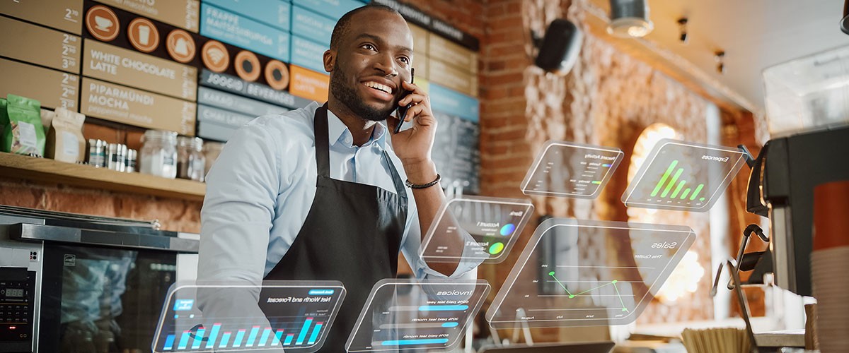 A smiling person in an apron stands in a bright kitchen, talking on the phone with a welcoming atmosphere.