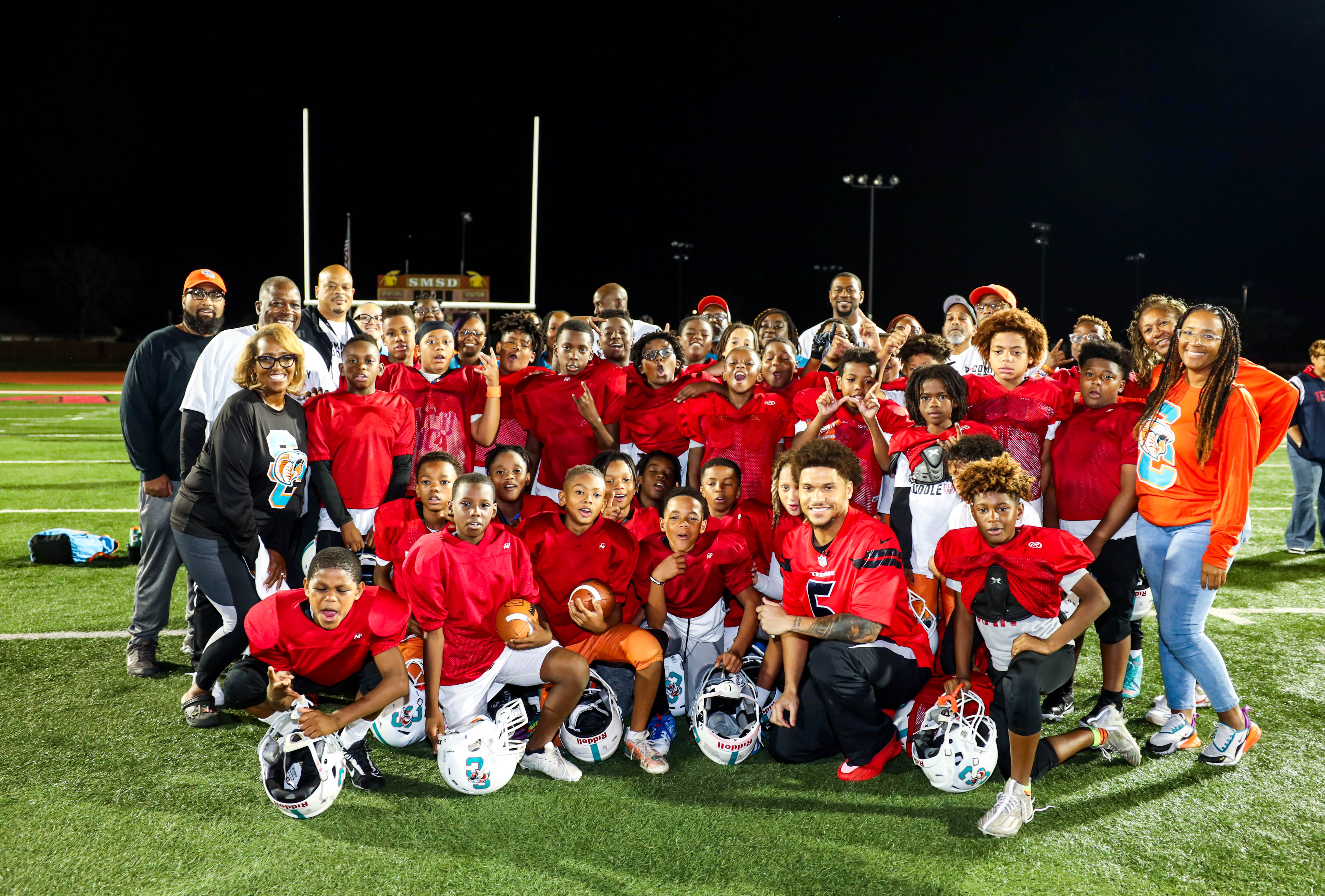 Youth football team posing together in uniform on the field, smiling proudly for a group photo.