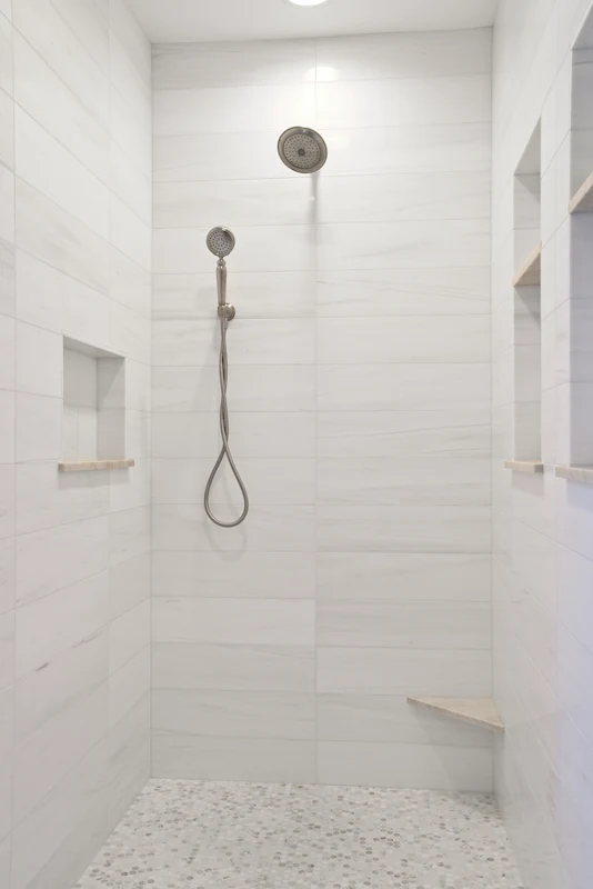 Close-up of the primary bathroom shower enclosure with elegant stone clad shower walls and built-in niches and corner foor stool style shelf from the Big Canyon Remodel project. Photo by Chris Darnall.
