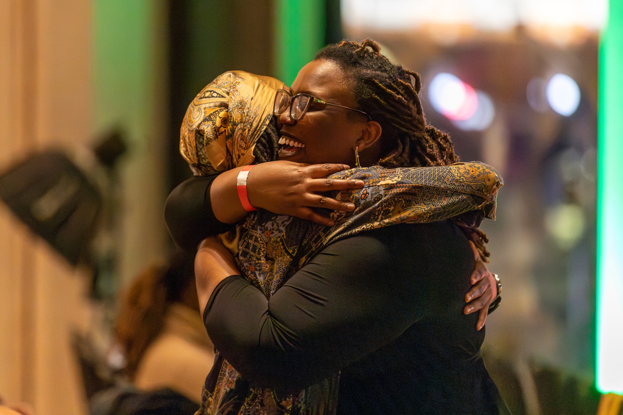 Two people warmly embrace in a joyful moment, both smiling in a brightly lit setting.
