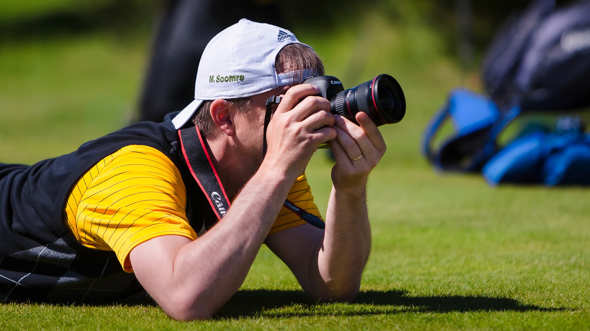 Mats Soomre lying on the grass at a golf tournament, photographing through a Canon lens. Cover image for article on photography and team coaching. Photo: Mikk Soomre