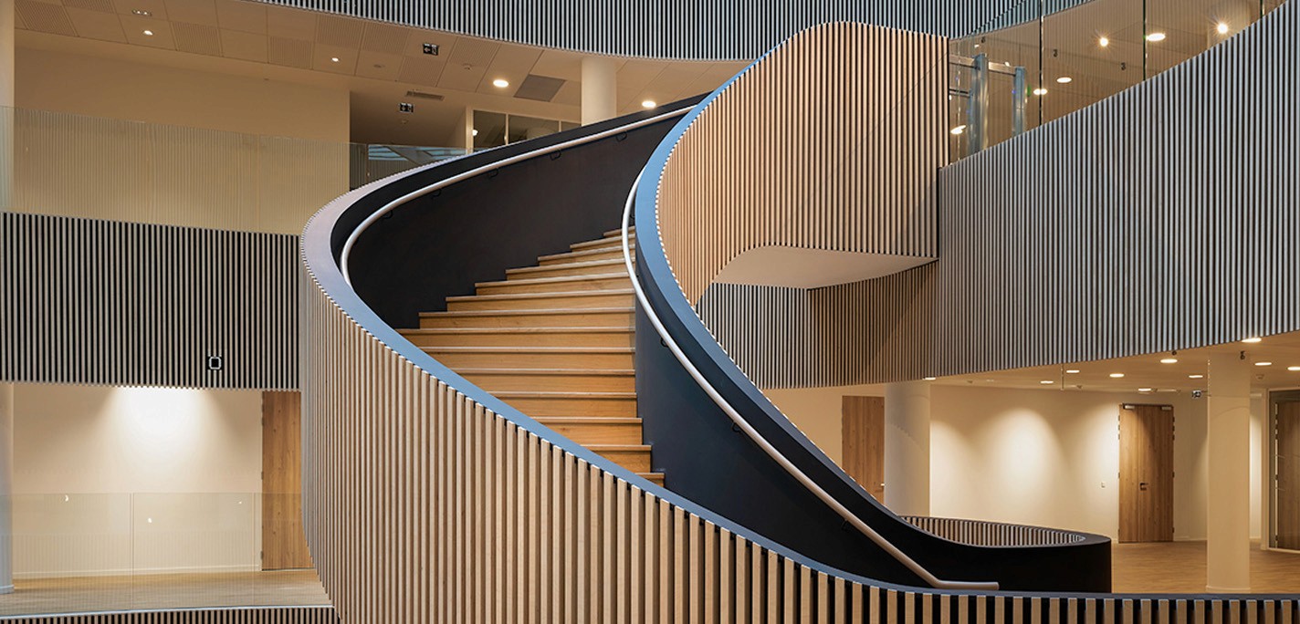 Escalier en colimaçon en bois clair et rampe noire dans un bâtiment moderne. Architecture intérieure design.