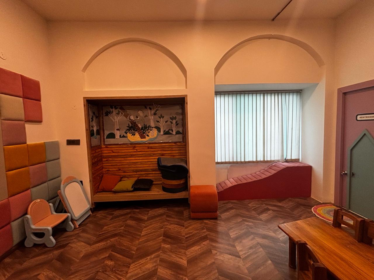 Arched Adventures: Twin architectural arches frame distinct activity zones—a cozy reading nook with a mural and a soft-play ramp by the window—creating a landscape of exploration for children.