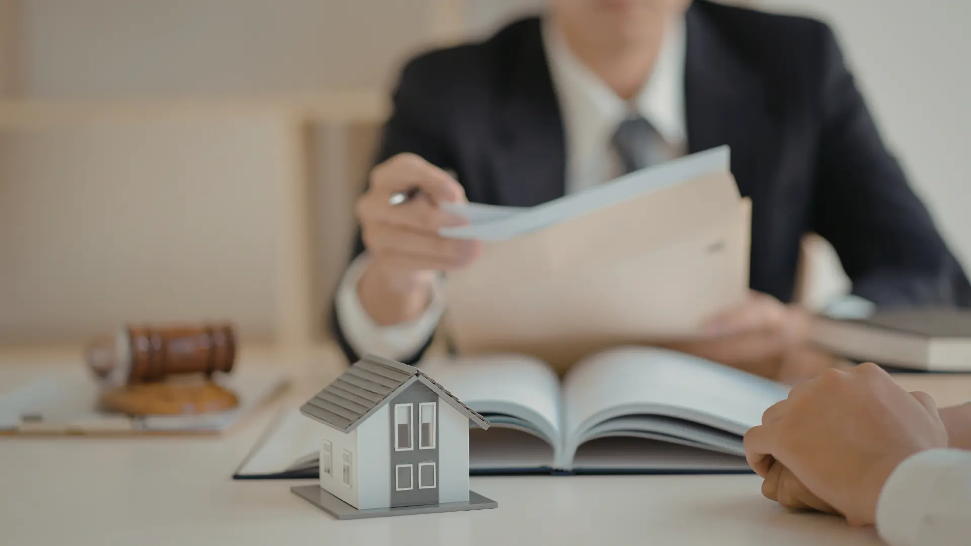 Immobilienberatung mit Vertragsunterlagen und Hausmodell auf Tisch bei Maklertermin