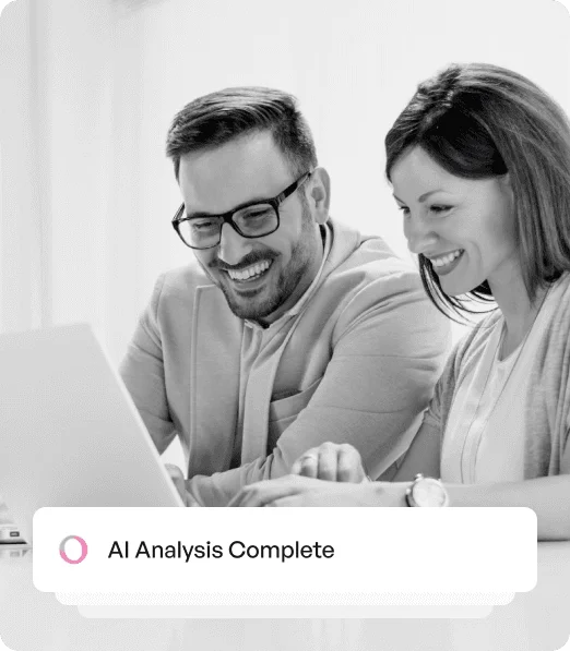 Two people sitting at a table are smiling and looking at a laptop screen, with a notification displaying "AI Analysis Complete."