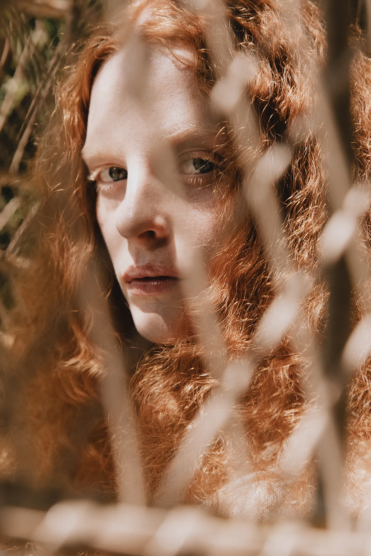 Close-up portrait of a red-haired model from the Annapurna SS26 campaign looking through a wire mesh fence.