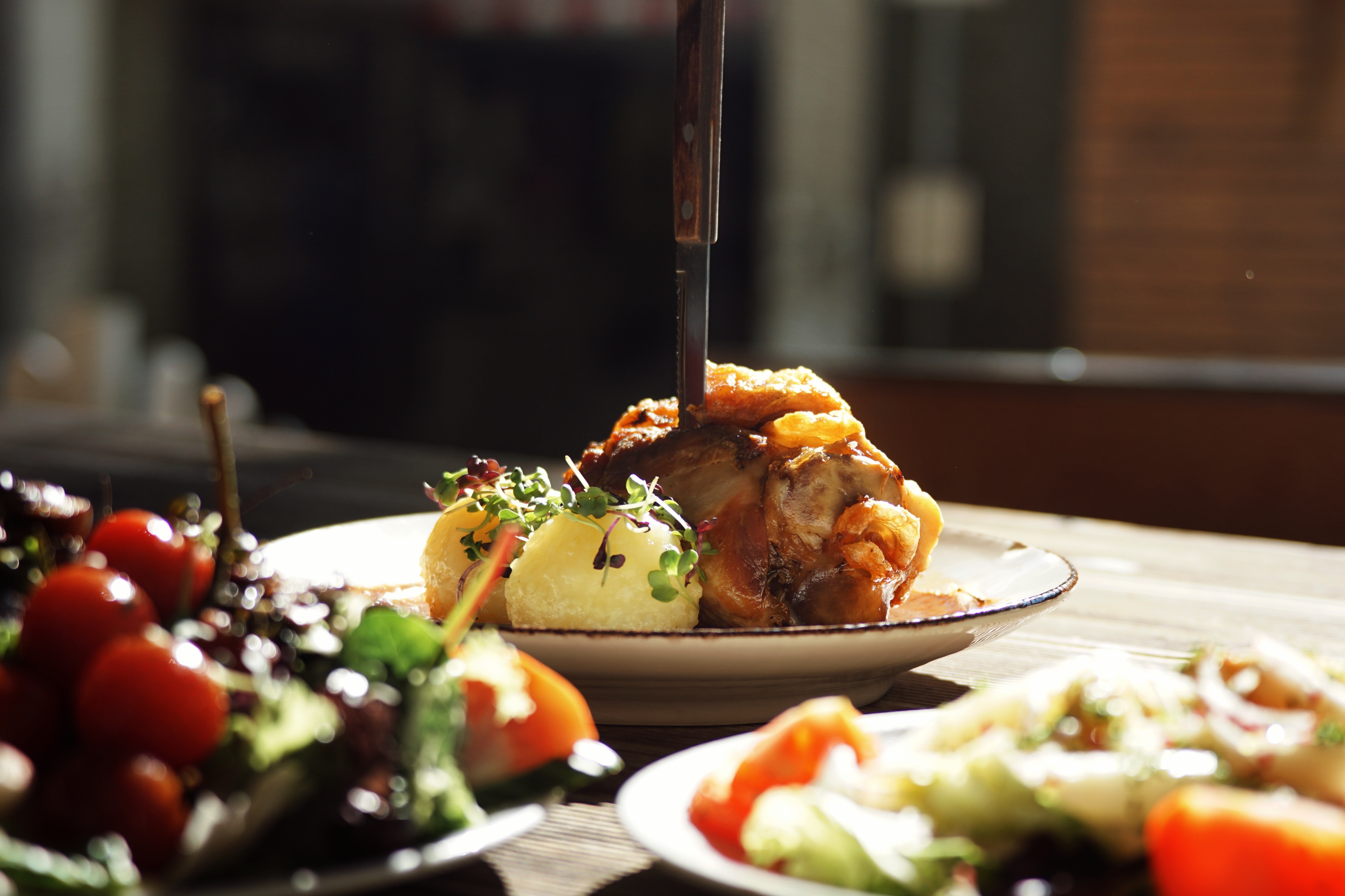 Schweinshaxe mit Knödel, davor zwei Salat, im Sonnenlicht