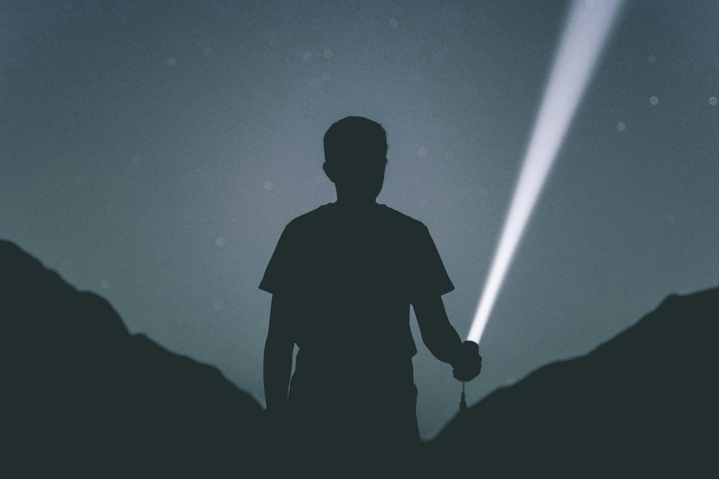 Silhouette of a person holding a flashlight at night.