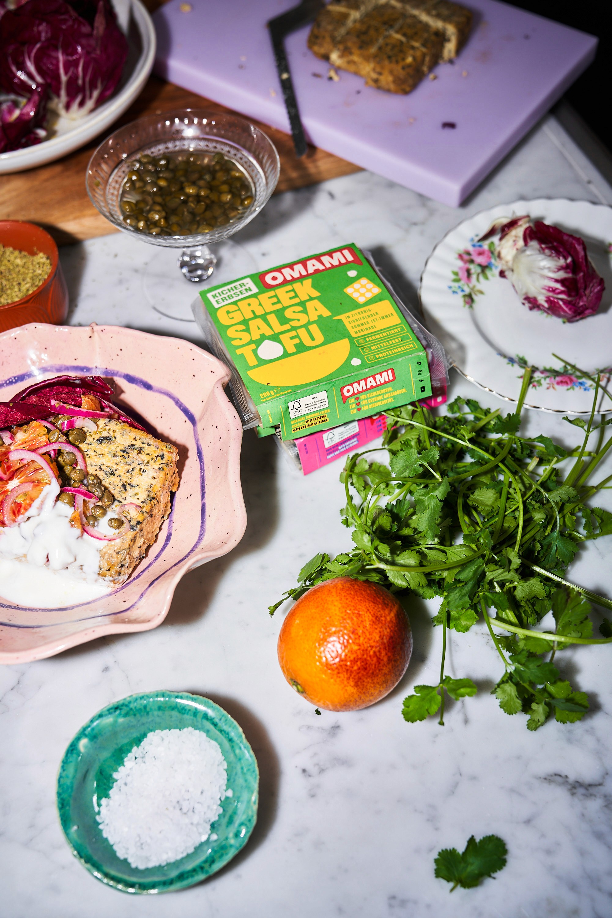 Green Salsa OMAMI Tofu laying on a white marble table surrounded by other ingredients