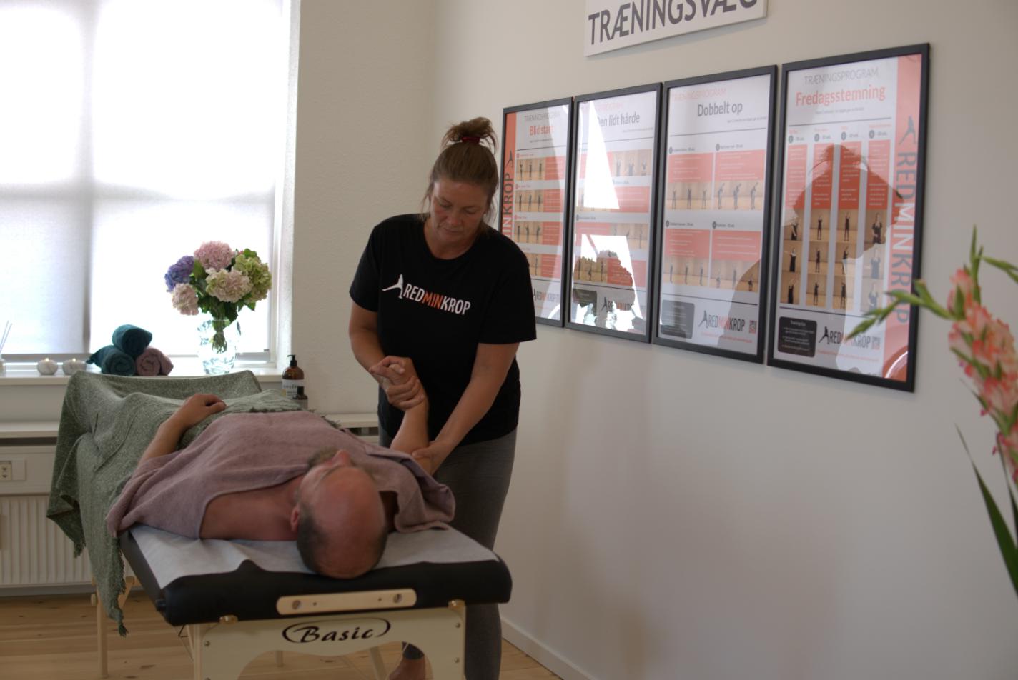 Firmamassage på arbejdspladsen, hvor en REDMINKROP-behandler masserer en persons arm på en massagebriks.