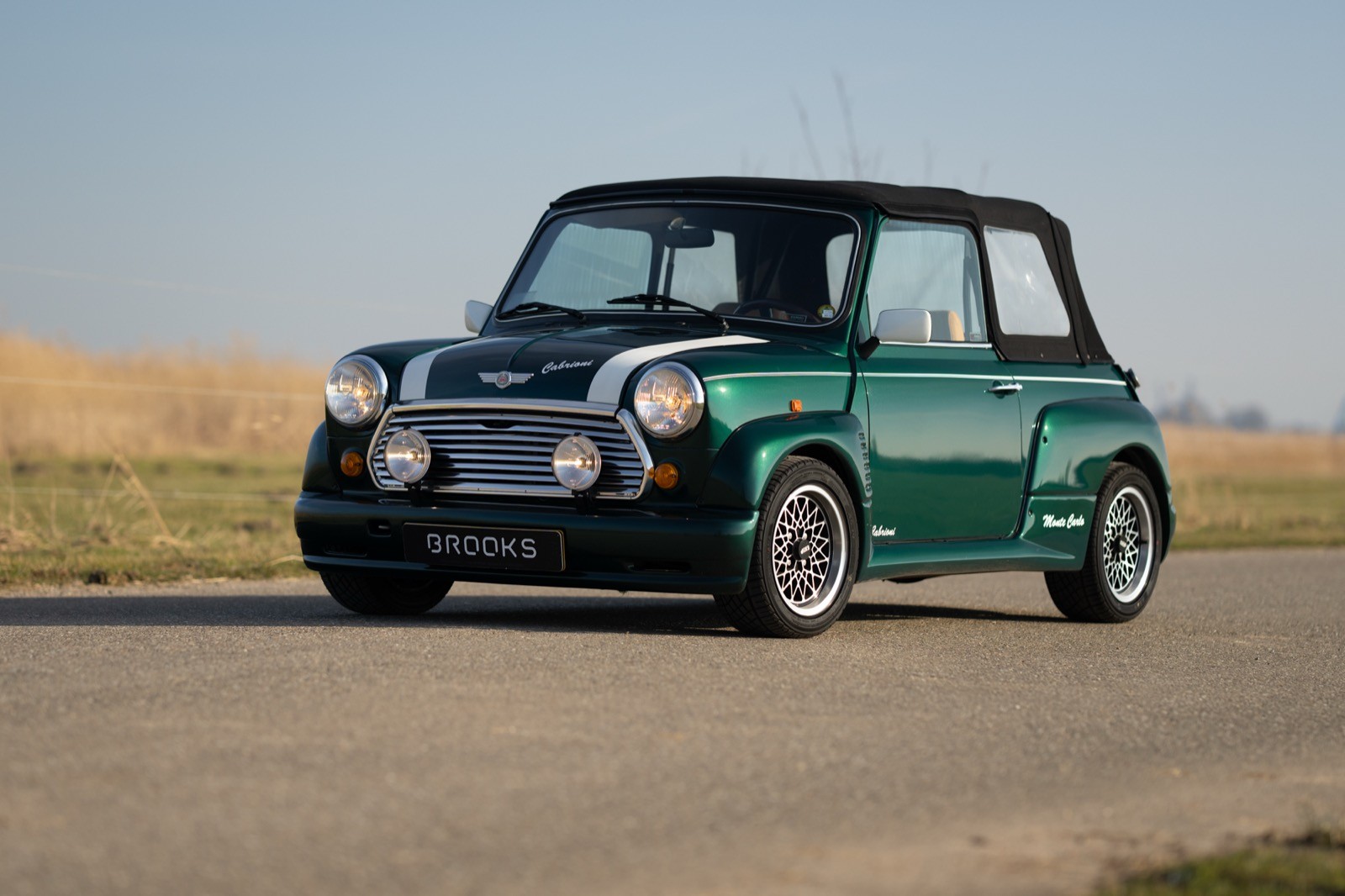 A vintage green and black car driving on a road with fields in the background under a clear blue sky.