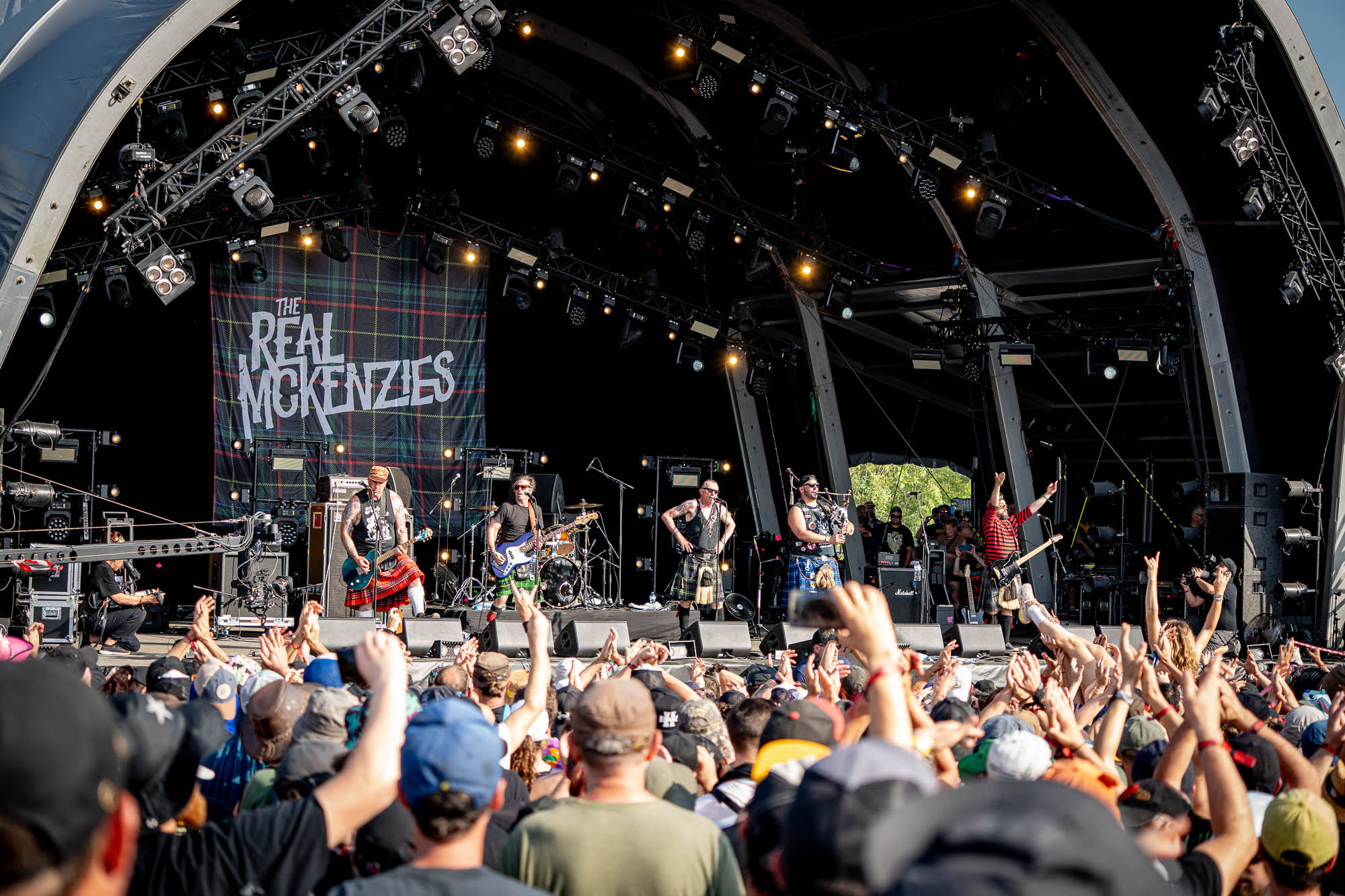 Groupe sur scène sous une bannière « The Real McKenzies », foule aux bras levés