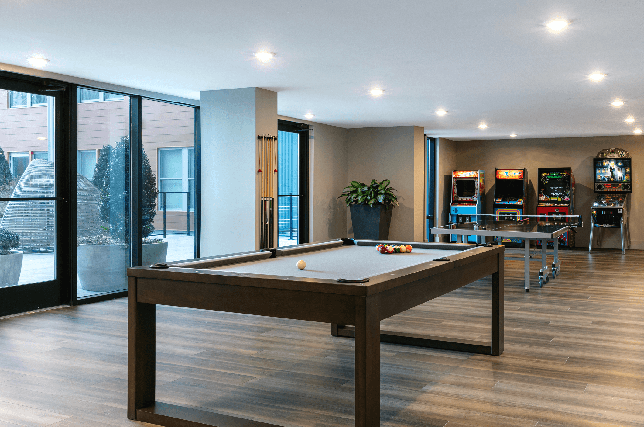 Modern game room with a pool table, large windows, and stylish decor, featuring natural light and a cozy atmosphere.