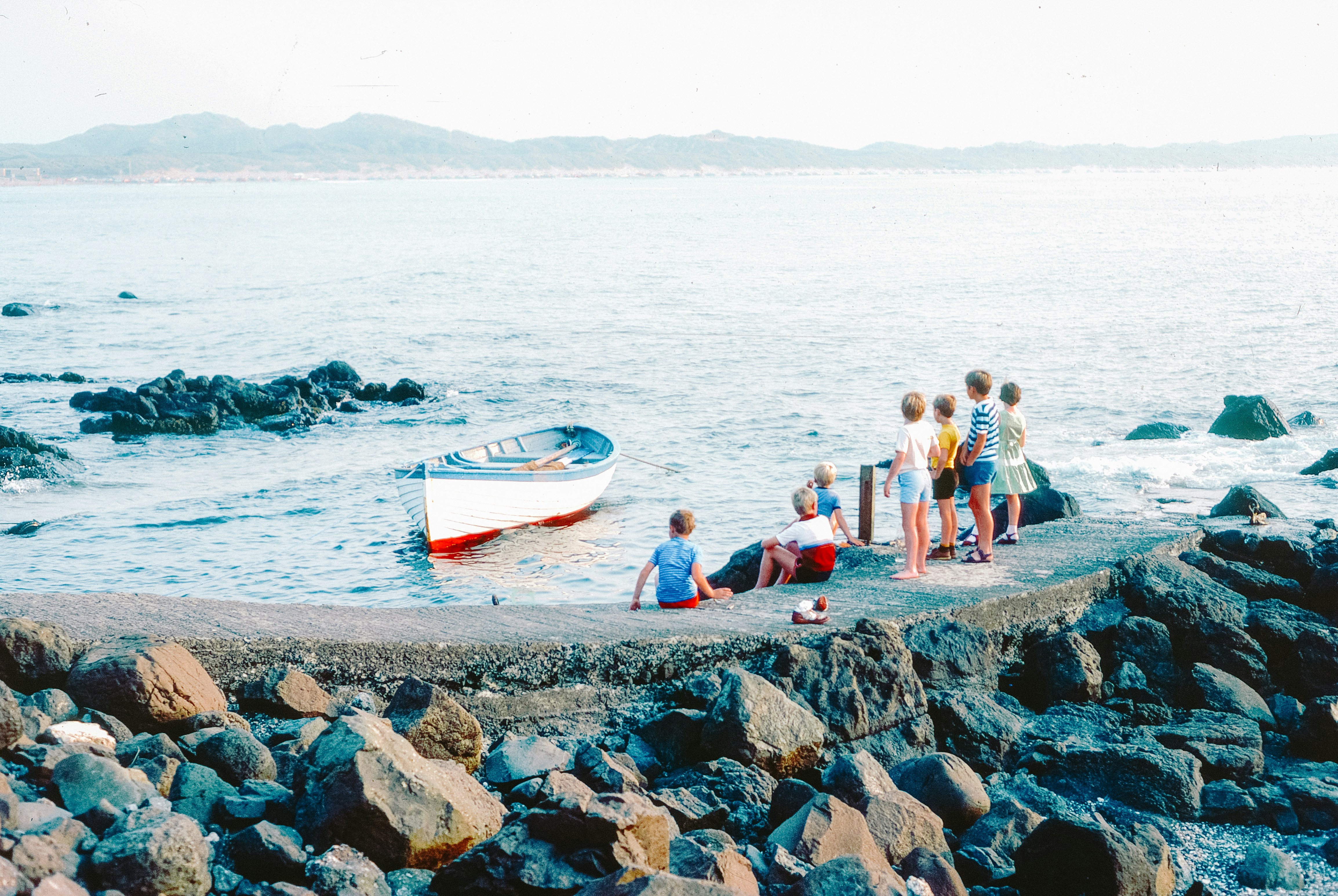 People gathered by a boat on a rocky shore