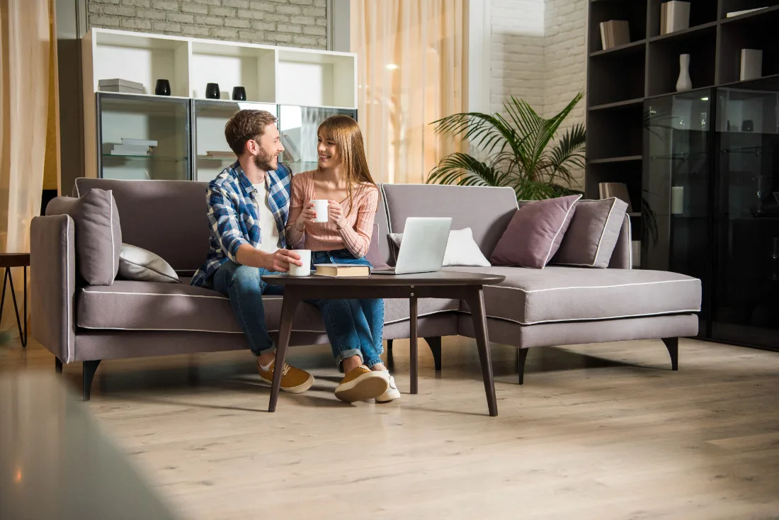 Couple sitting on couch looking at each other holding mugs. 
