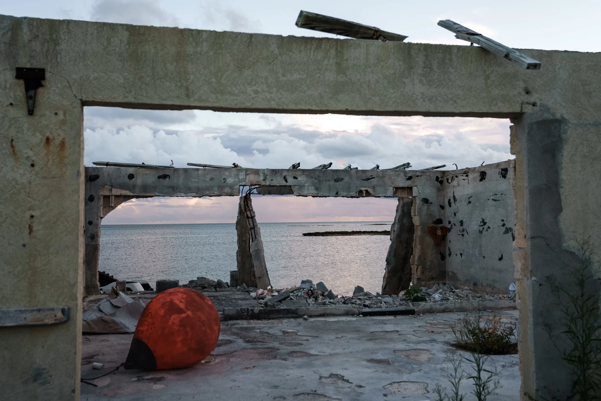 View through a dilapidated structure showing the sea, with scattered debris and a large red buoy on the ground.