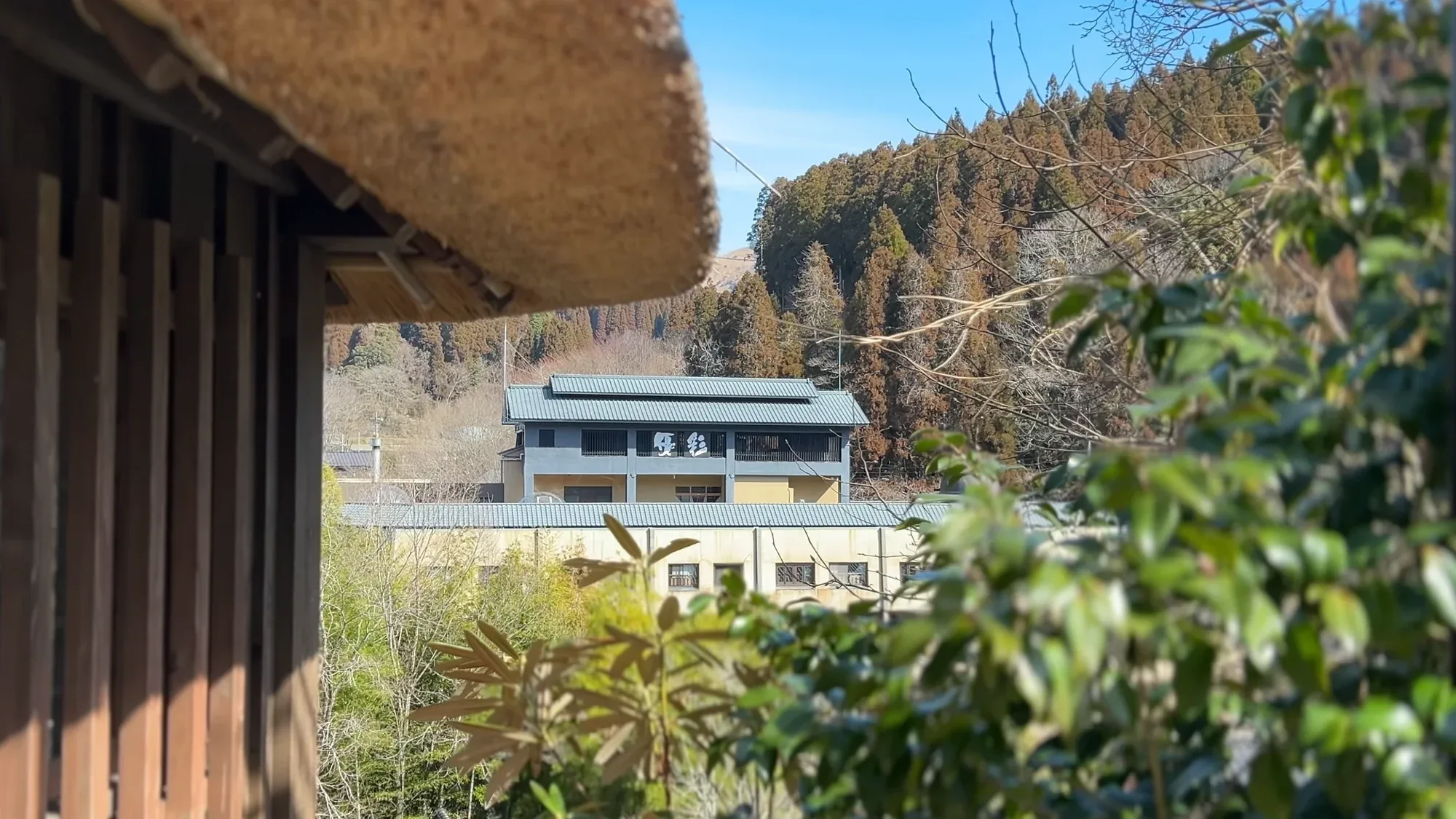 A thatched eave at Kurokawa Onsen framing a white inn across the valley