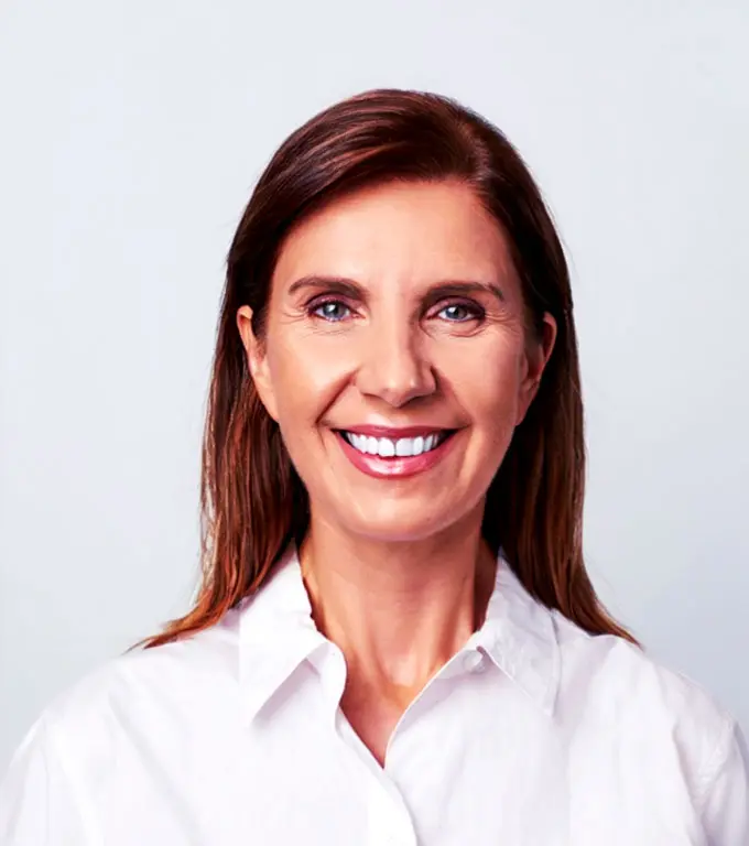 Woman with brown hair smiling in a white collared shirt.