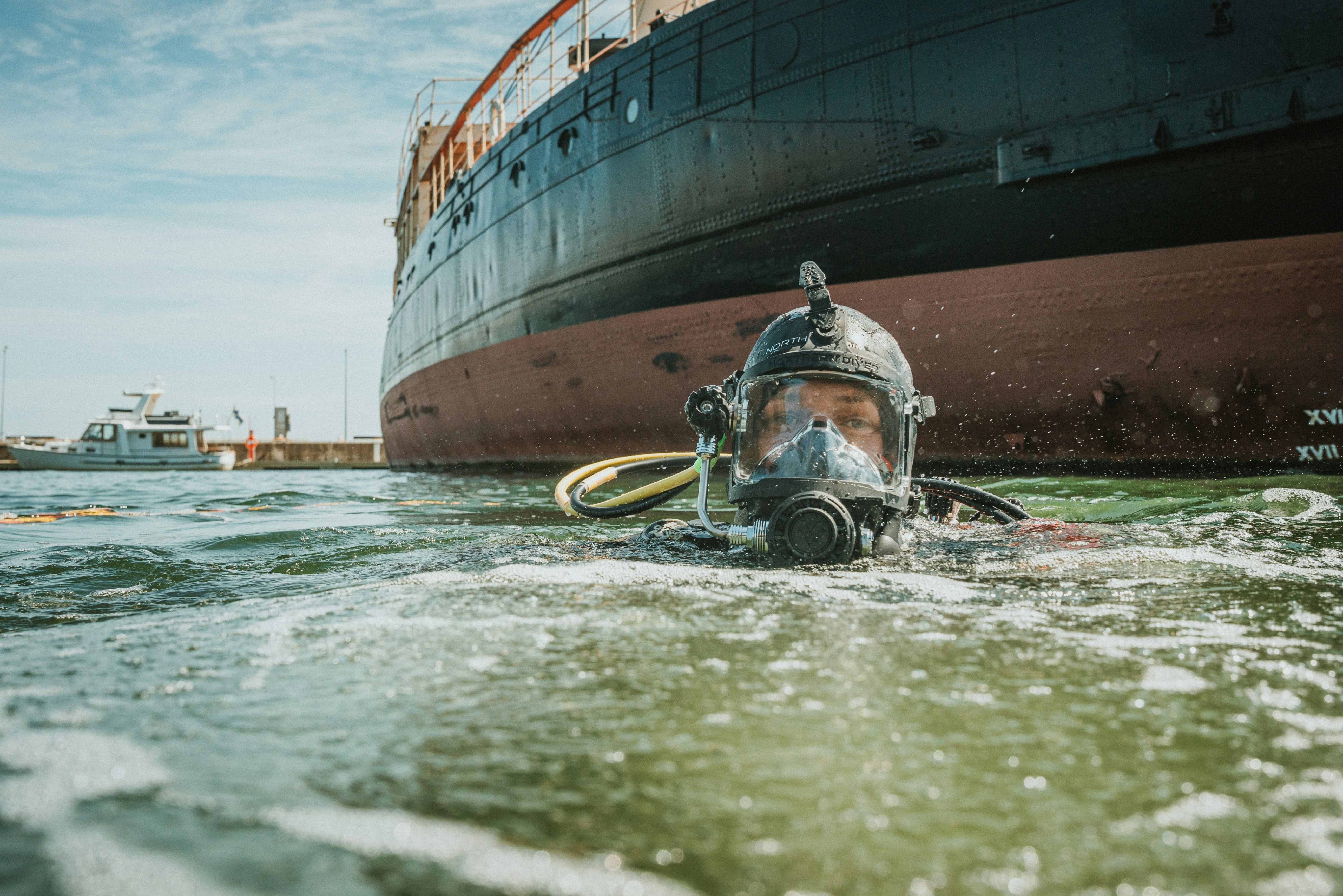 Commercial diver performing underwater hull cleaning and propeller polishing to reduce biofouling drag on a vessel.