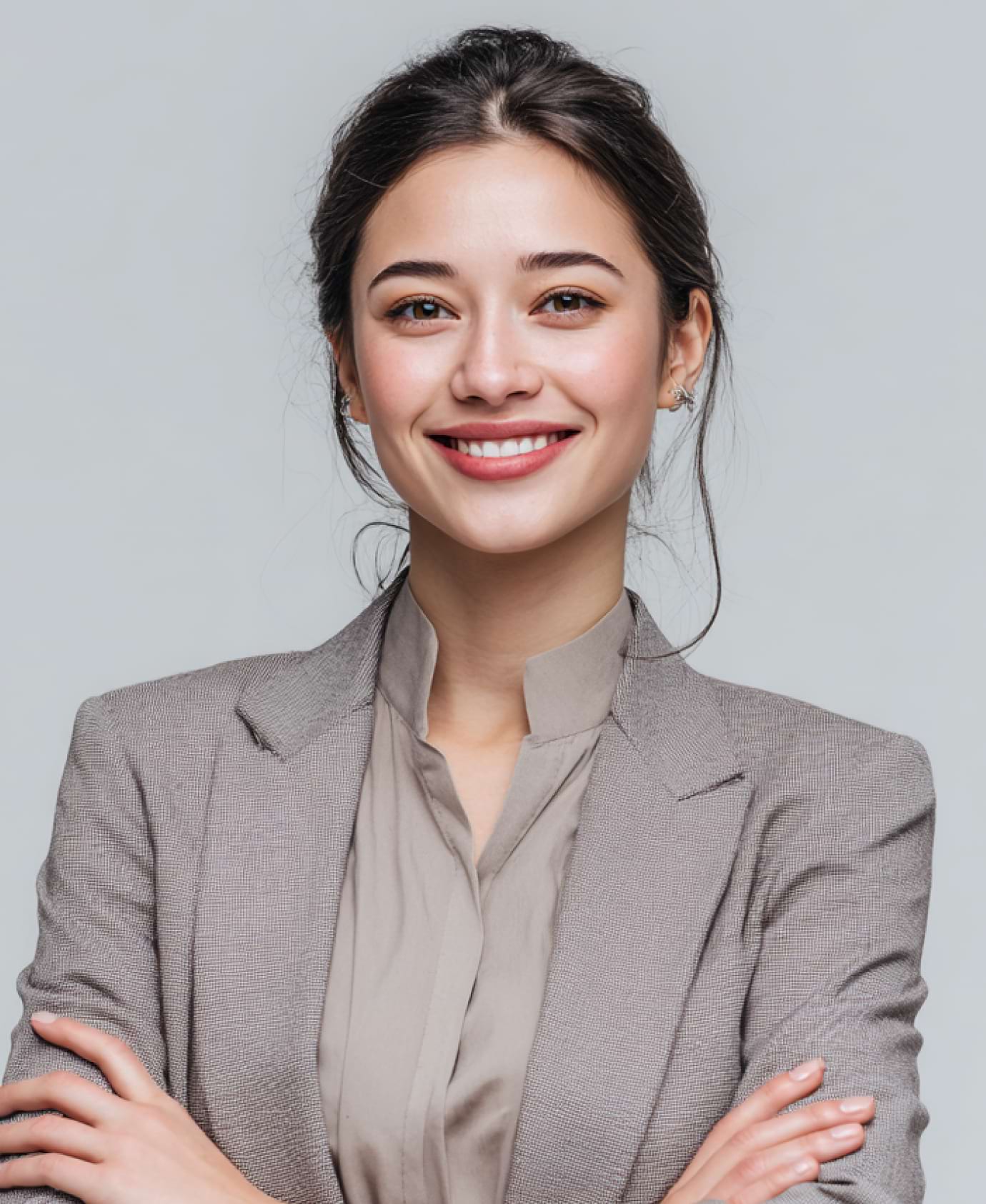 Smiling woman in a gray blazer and beige shirt, with arms crossed. She exudes confidence against a plain background. Her hair is neatly tied back.
