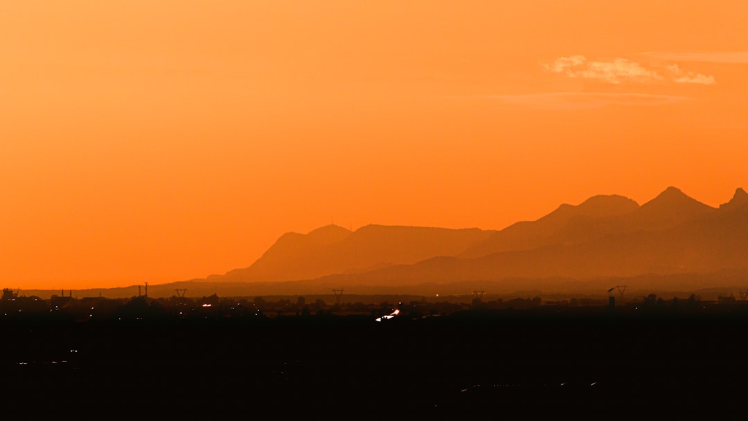Desert mountain silhouettes glowing against a deep orange sunset sky at dusk.