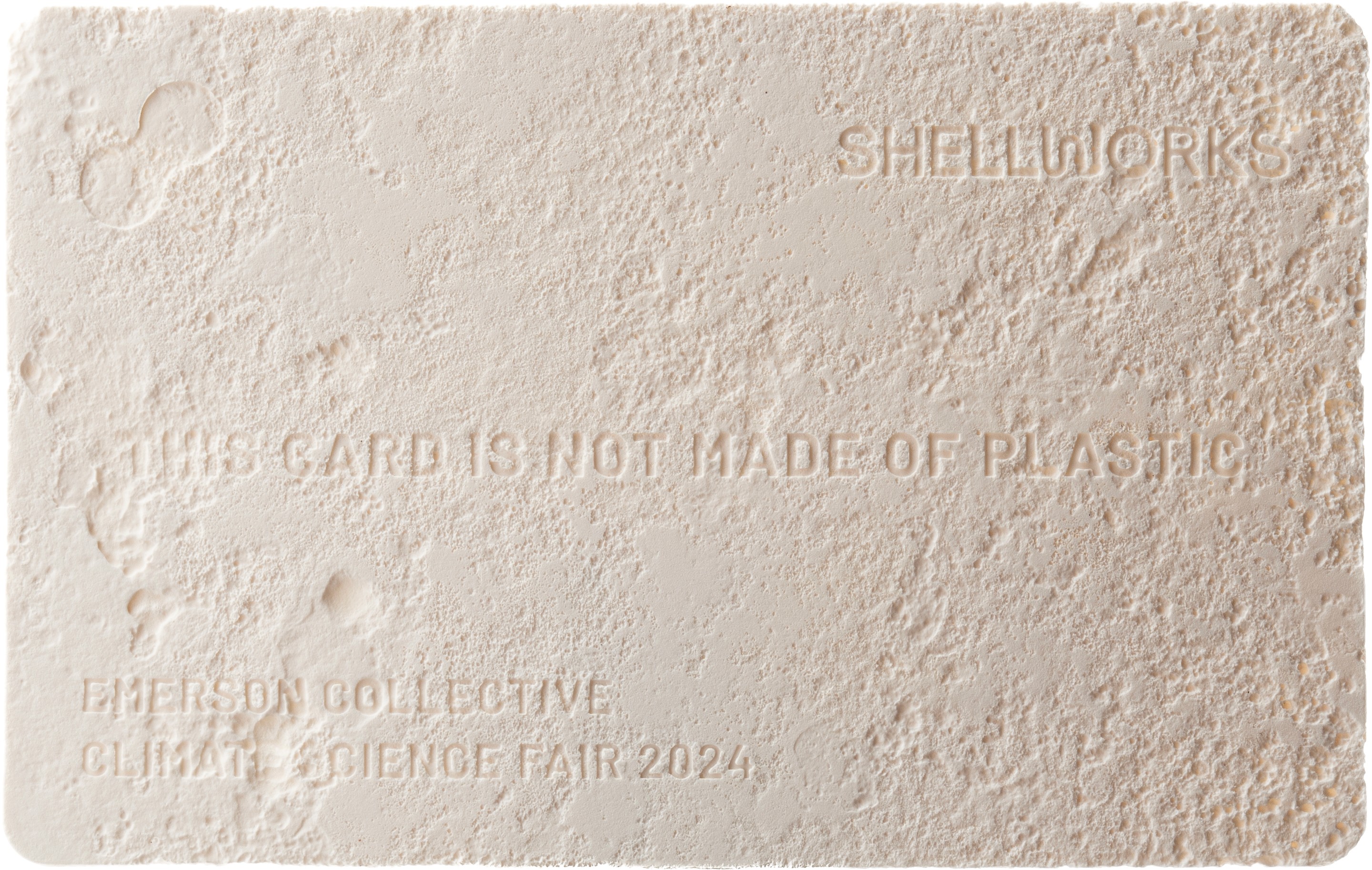 A Shellworks business card made of Vivomer material featuring the text 'this card is not made of plastic,' shown partially composted in garden soil to prove its plastic-free, biodegradable nature.