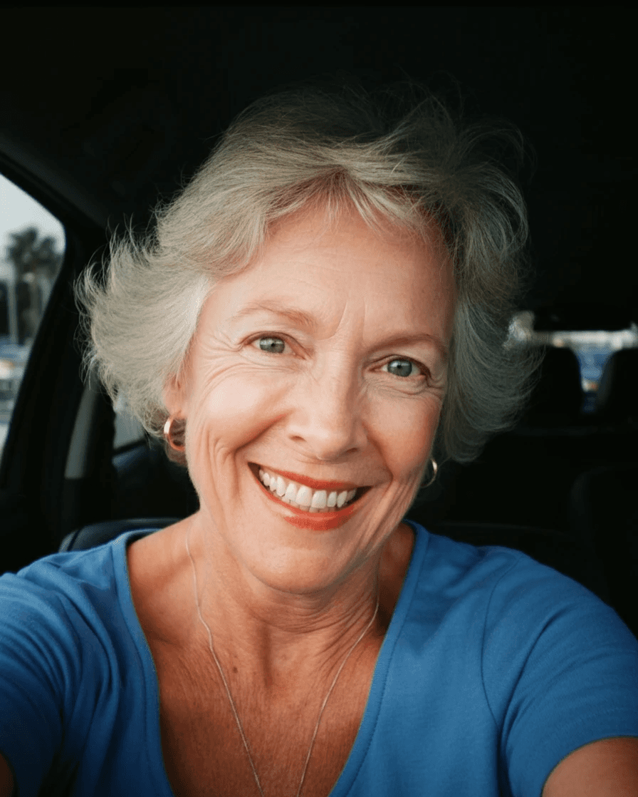 Smiling older woman with short, gray hair, wearing a blue shirt. She's illuminated by sunlight, with red lipstick.