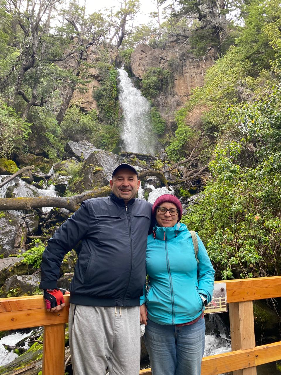Mujer sentada sobre un tronco frente a una cascada doble en un bosque frondoso de Argentina.