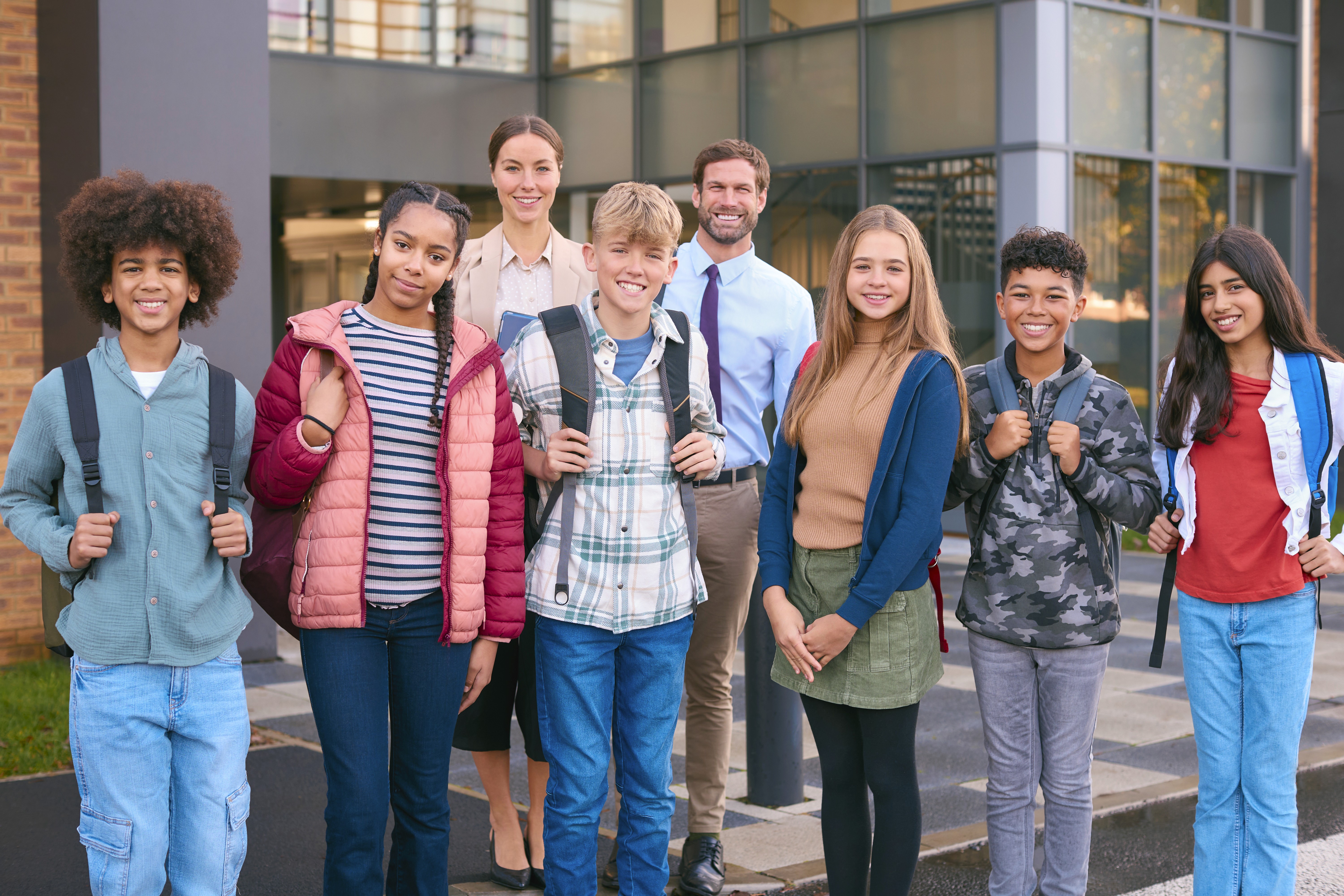 A photograph of happy students and teachers standing outside of a school. Smiles and joy are reactions given by students and teachers when they feel safe.