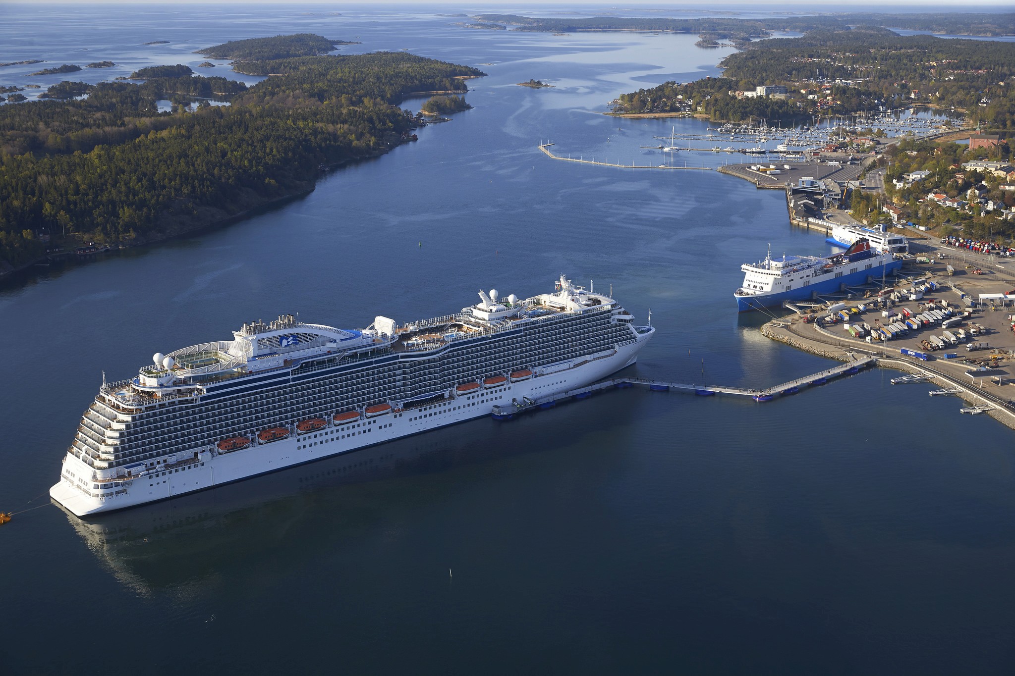 Aerial view of a cruise ship docked at a floating pier in Nynäshamn, Sweden, connecting the vessel to port facilities and surrounding archipelago waters.