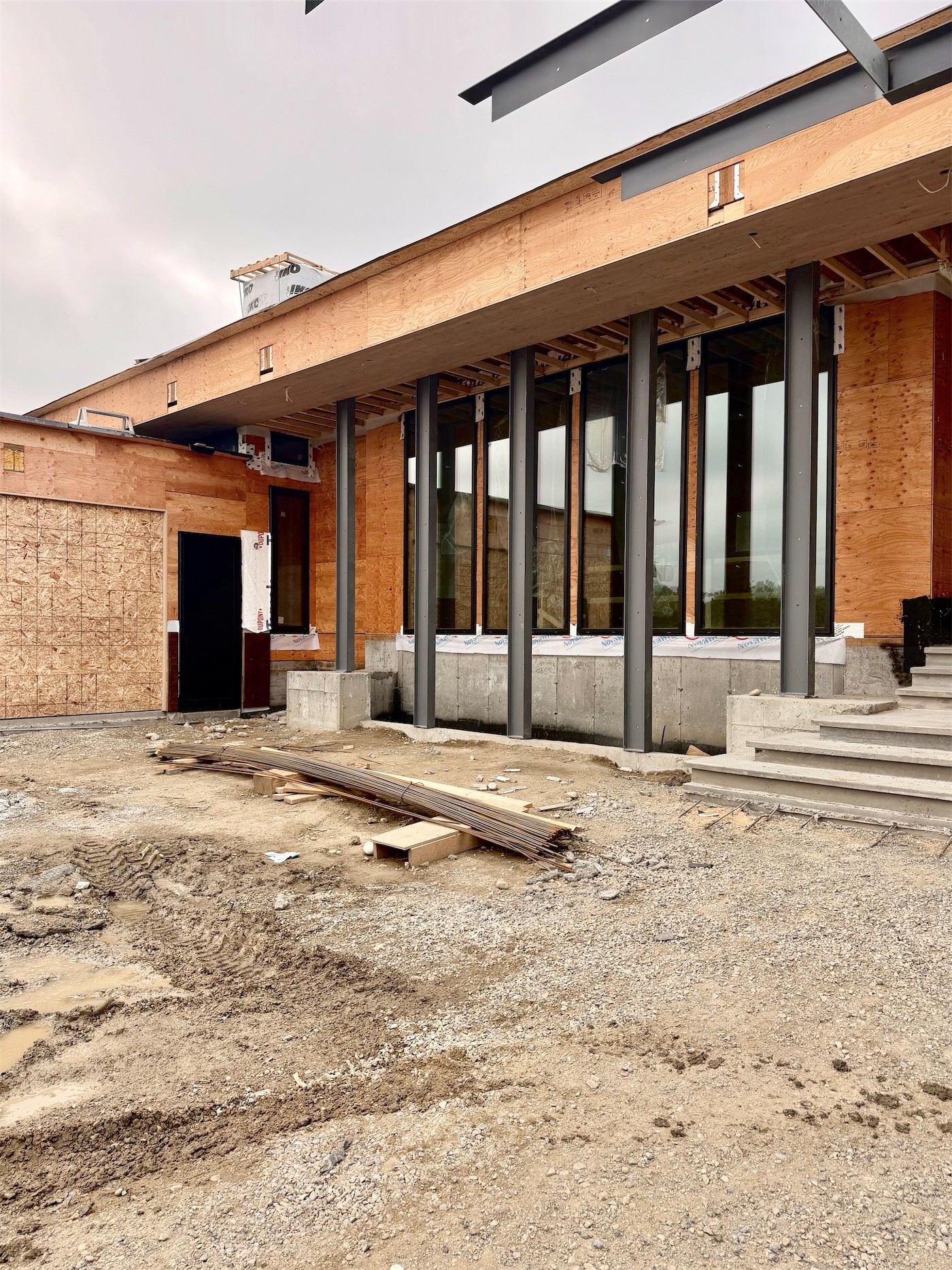 The plywood-clad exterior with steel columns and tall windows, under construction