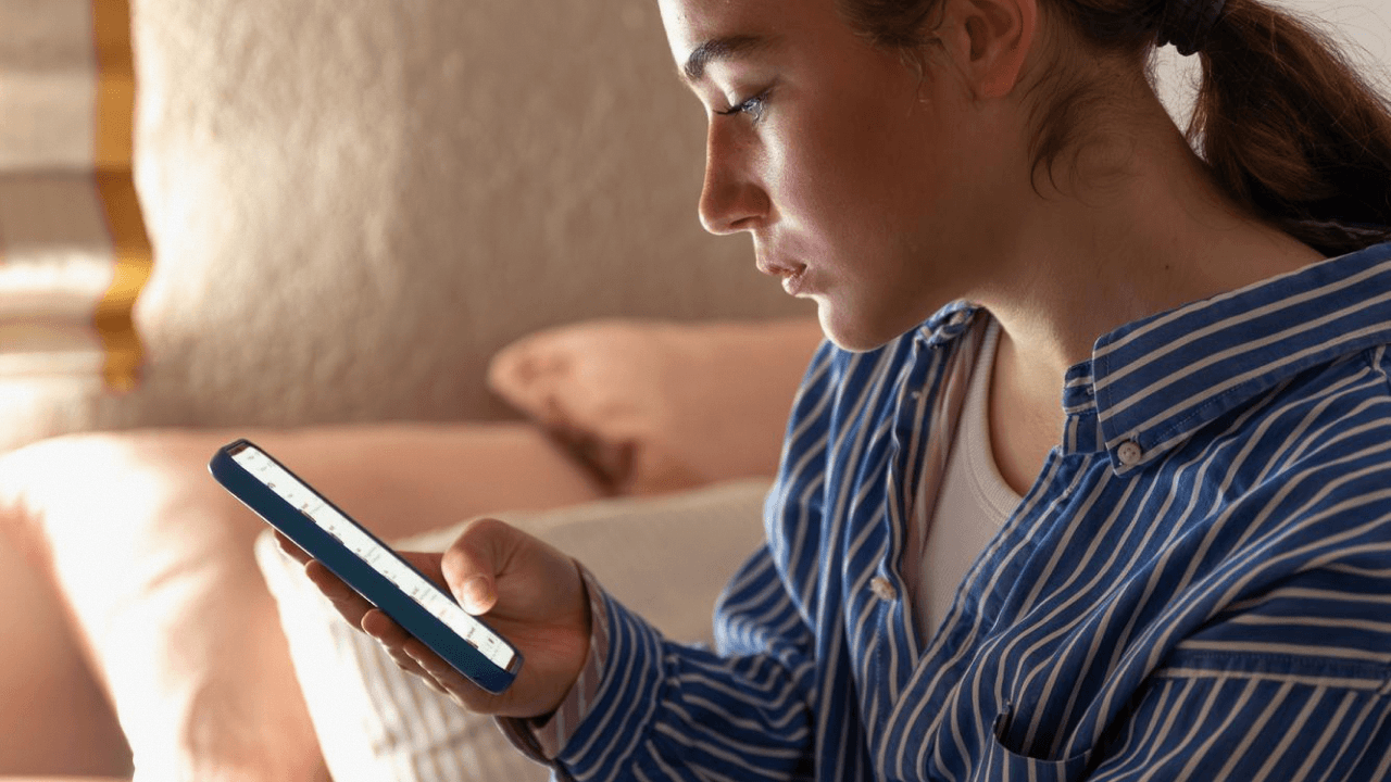 Femme sur un canapé consultant son téléphone avec une expression préoccupée