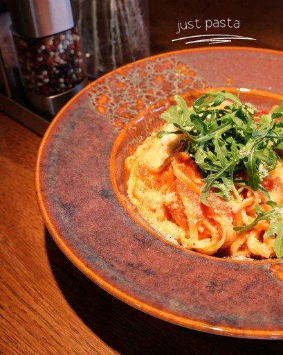 A plated pasta dish with tomato-based sauce, grated cheese, and fresh arugula, served on a rustic ceramic plate.