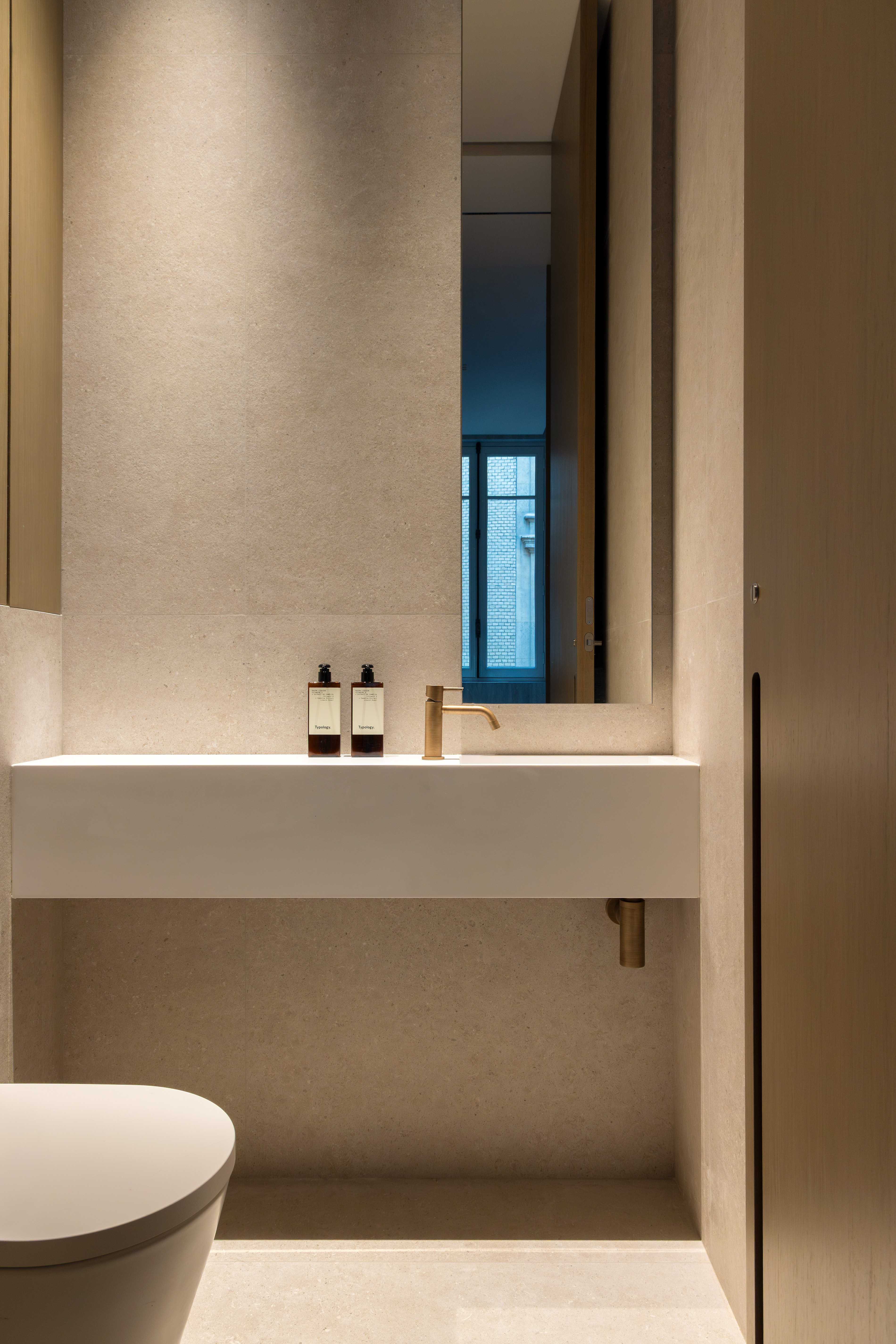 Toilettes avec lavabo integre, WC suspendu, robinetterie doree et placard en bois clair au-dessus
