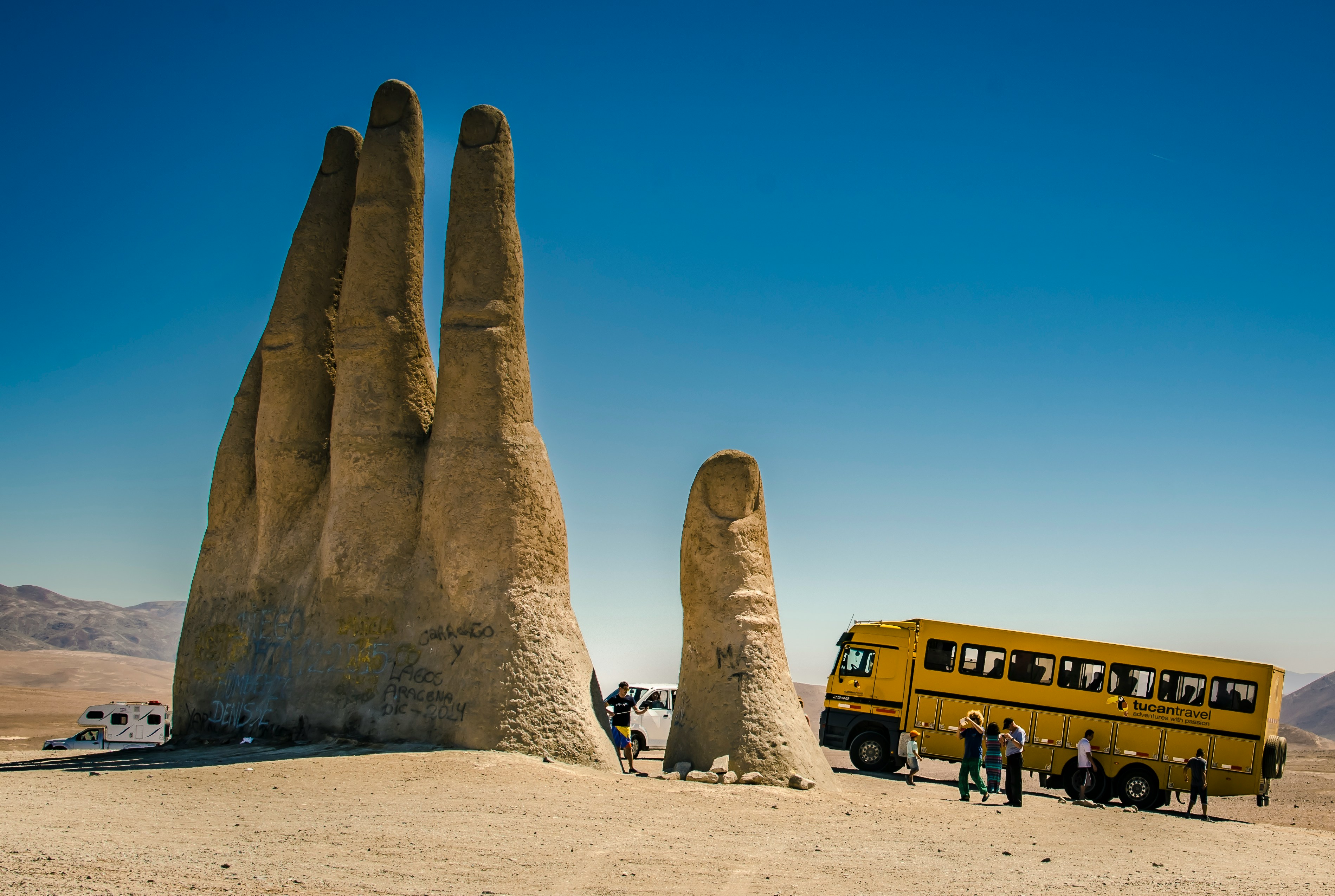 people sitting on brown sand near yellow bus during daytime
