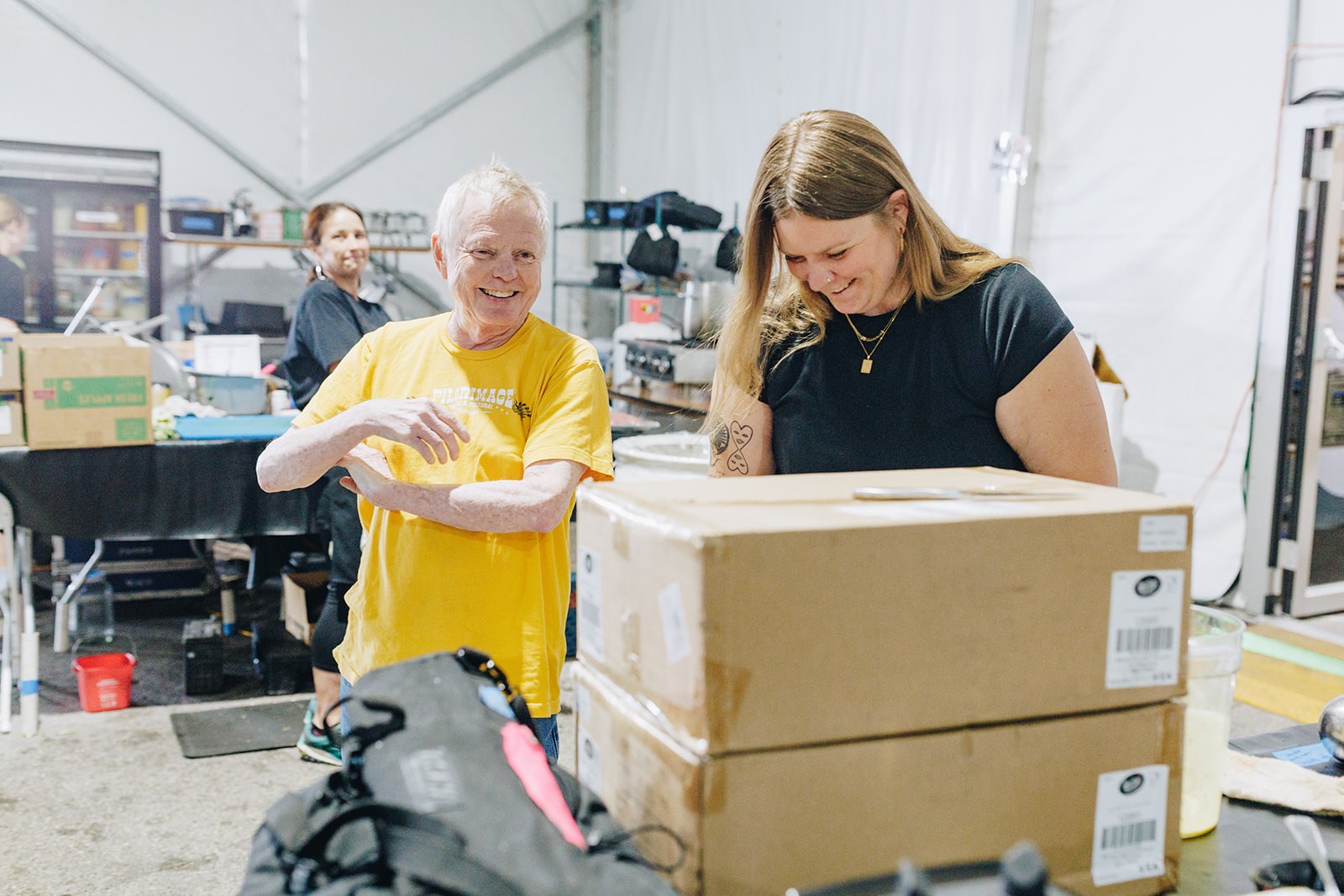 Two people are working together in a warehouse, unpacking boxes and organizing items in a workspace.