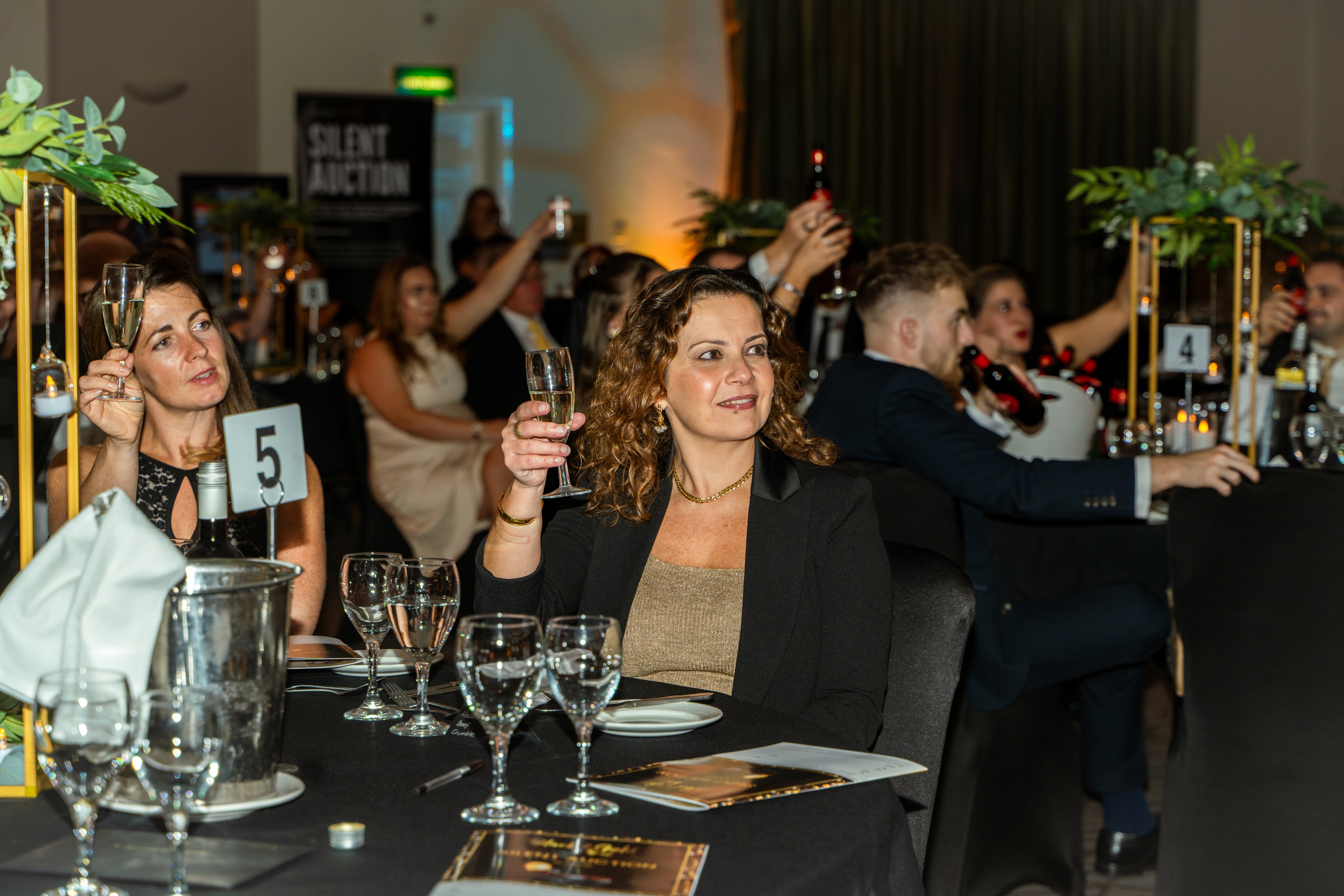 Woman holding a glass of wine at a black tie event with crowd in the background