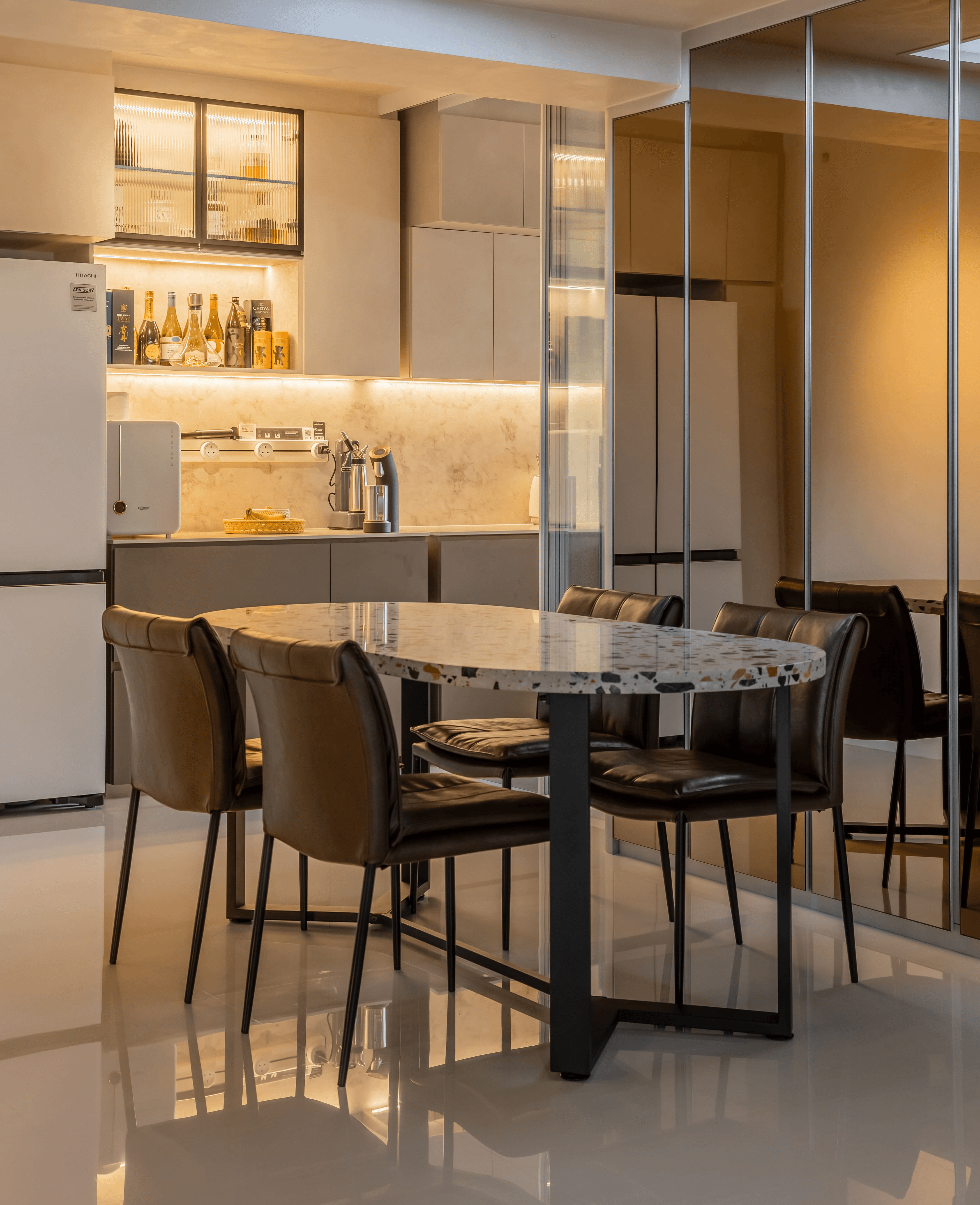 Modern dining area with terrazzo-style table, leather chairs, and mirrored cabinetry reflecting a sleek kitchen setup