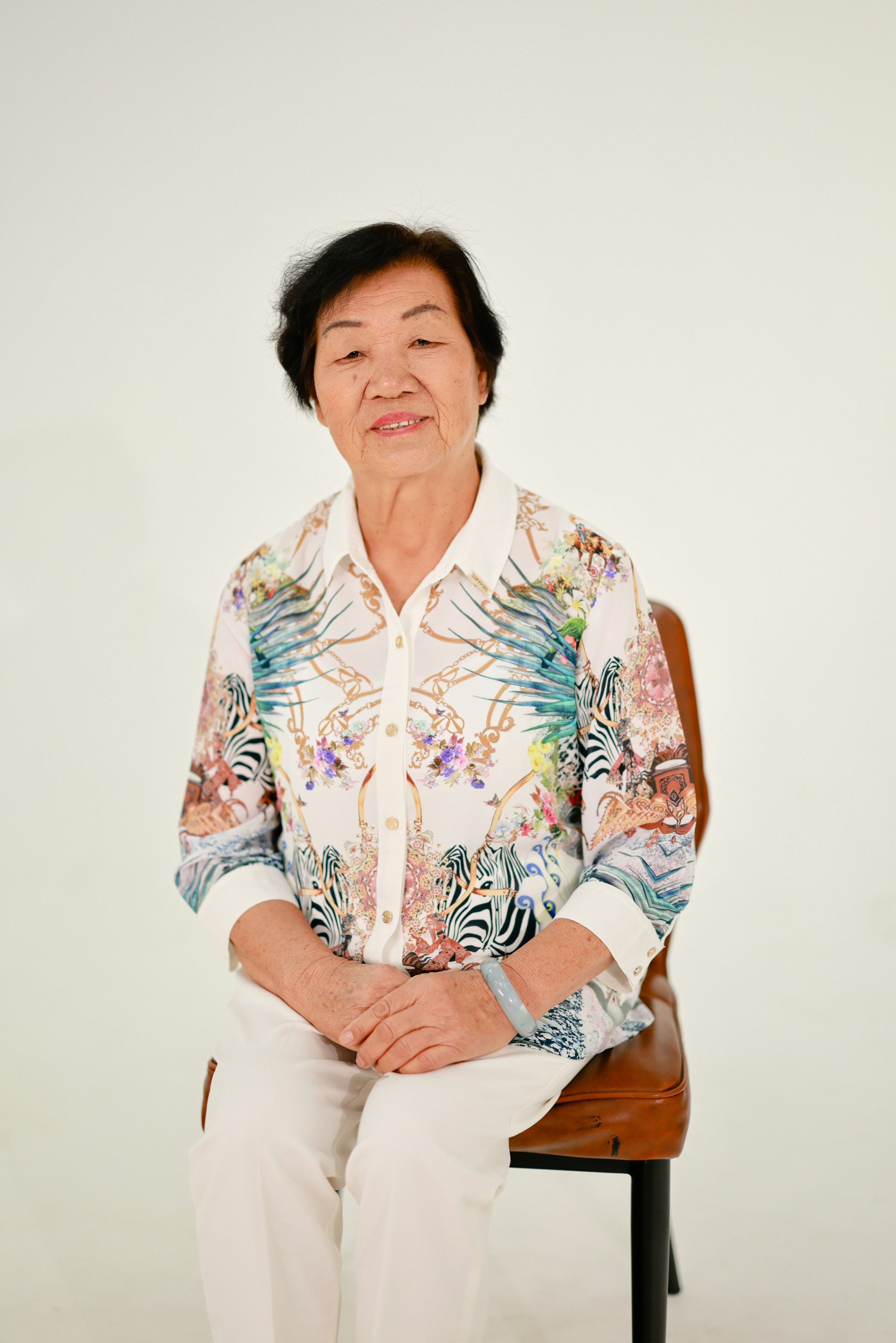 An elderly asian woman sits on a chair.