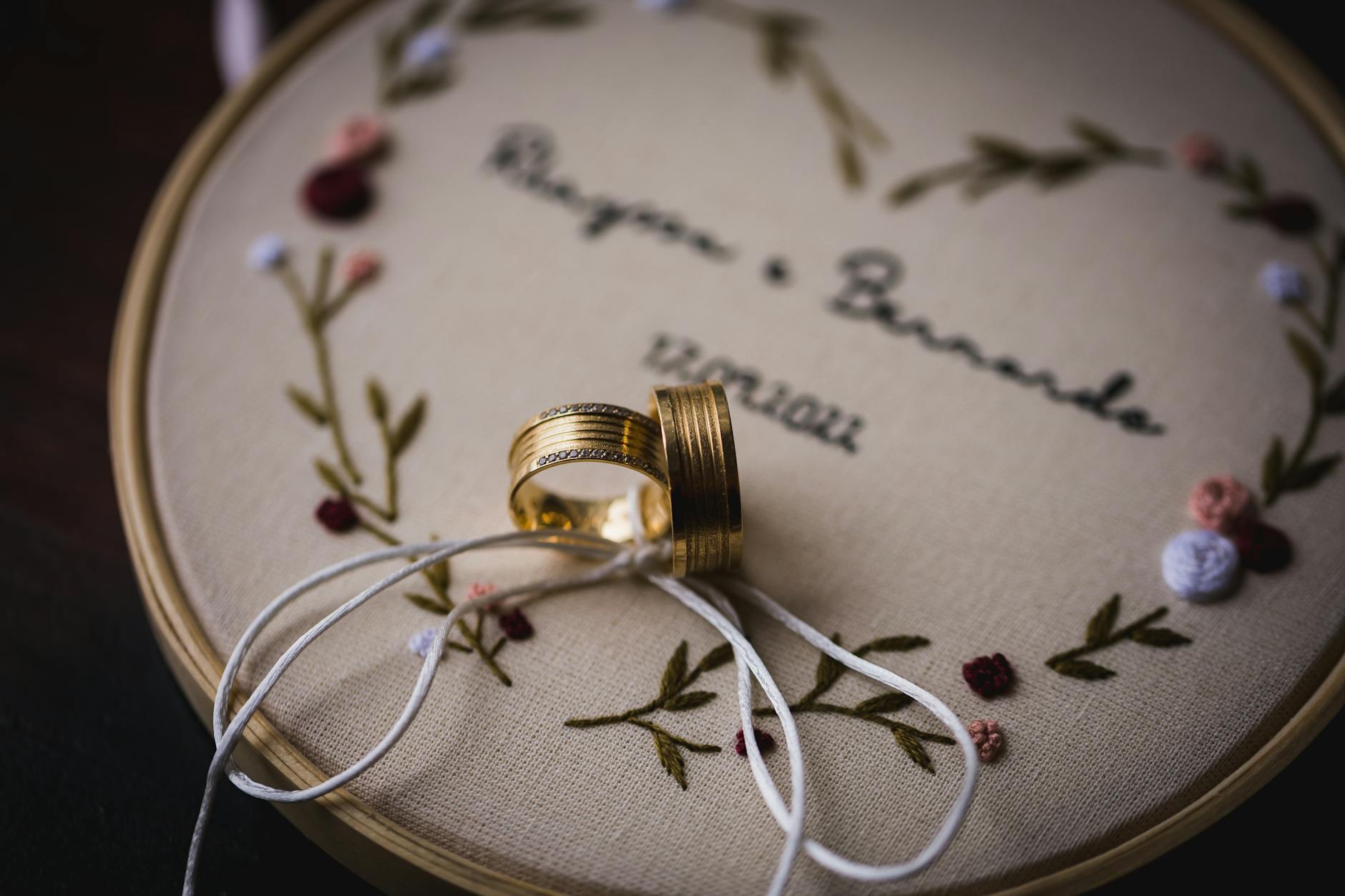 Close-up of wedding rings placed on beautifully embroidered fabric with floral details. Ideal for wedding themes.