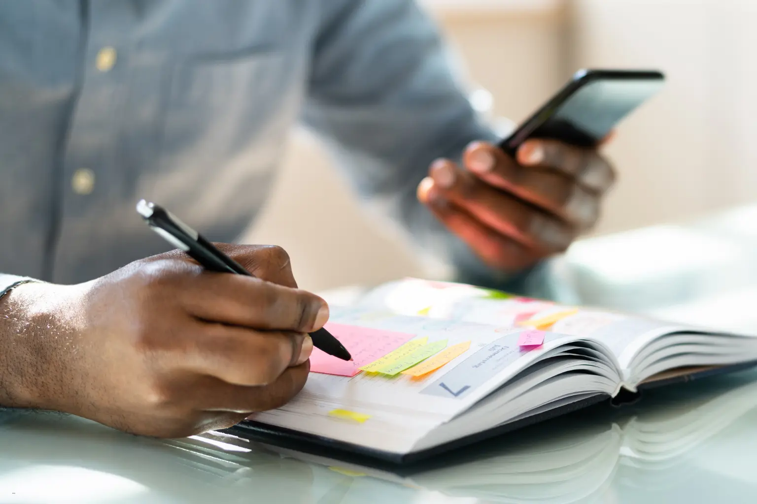 Scheduling automation for teams with a person using a smartphone and writing notes in a planner with sticky notes.